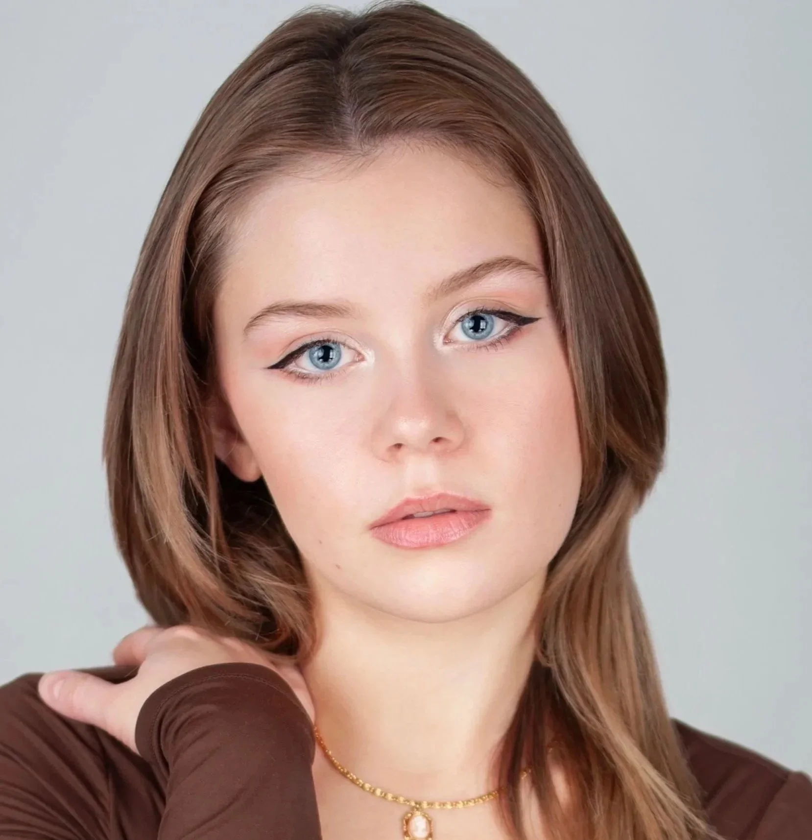 Lizzie Matlock, a young actress with auburn hair and blue eyes looking directly at the camera, wearing a brown top and a gold necklace with a pearl pendant.