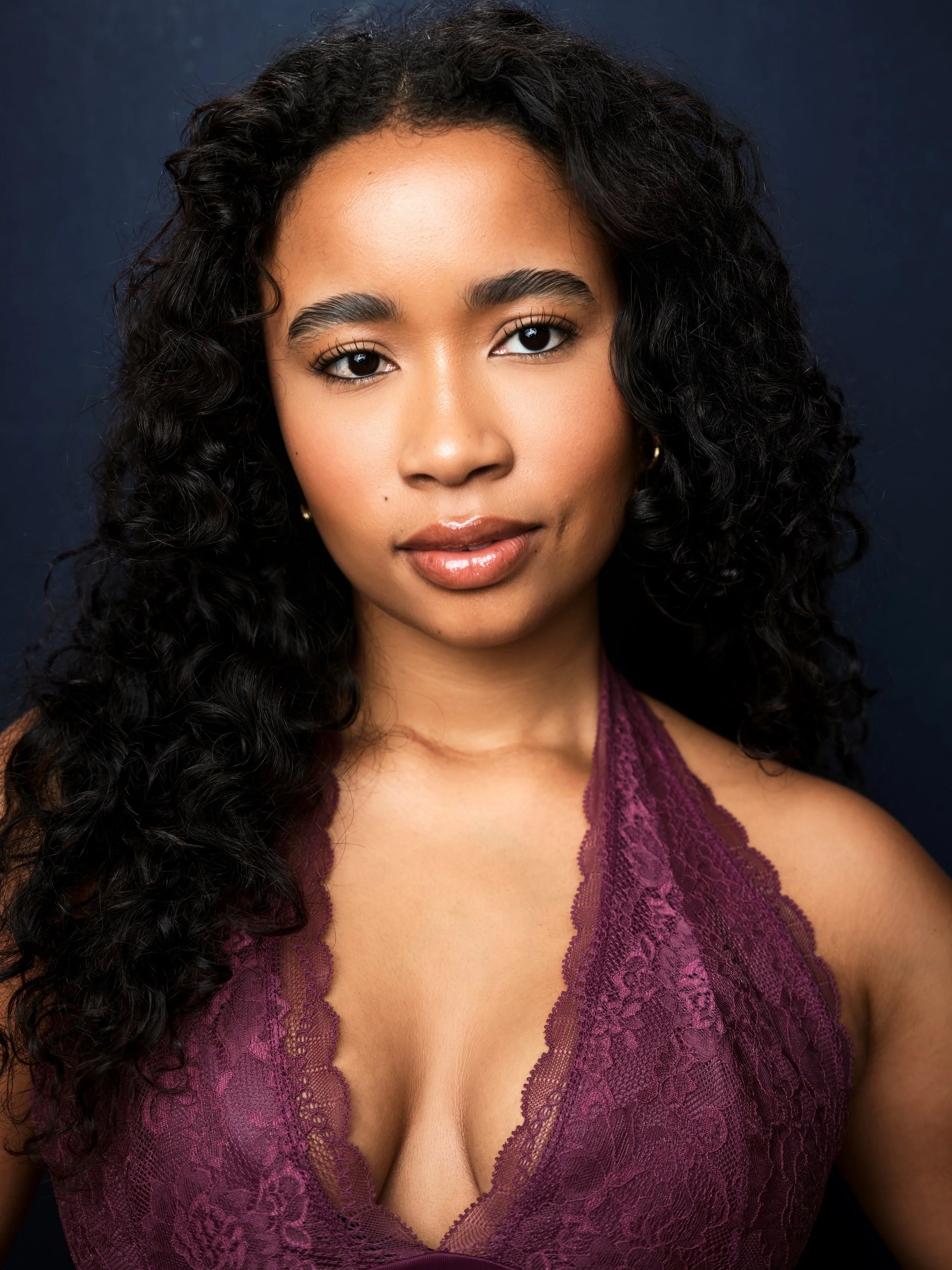 Tuesday Usry, a young actress with dark curly hair and dark brown eyes in a purple top against a navy background