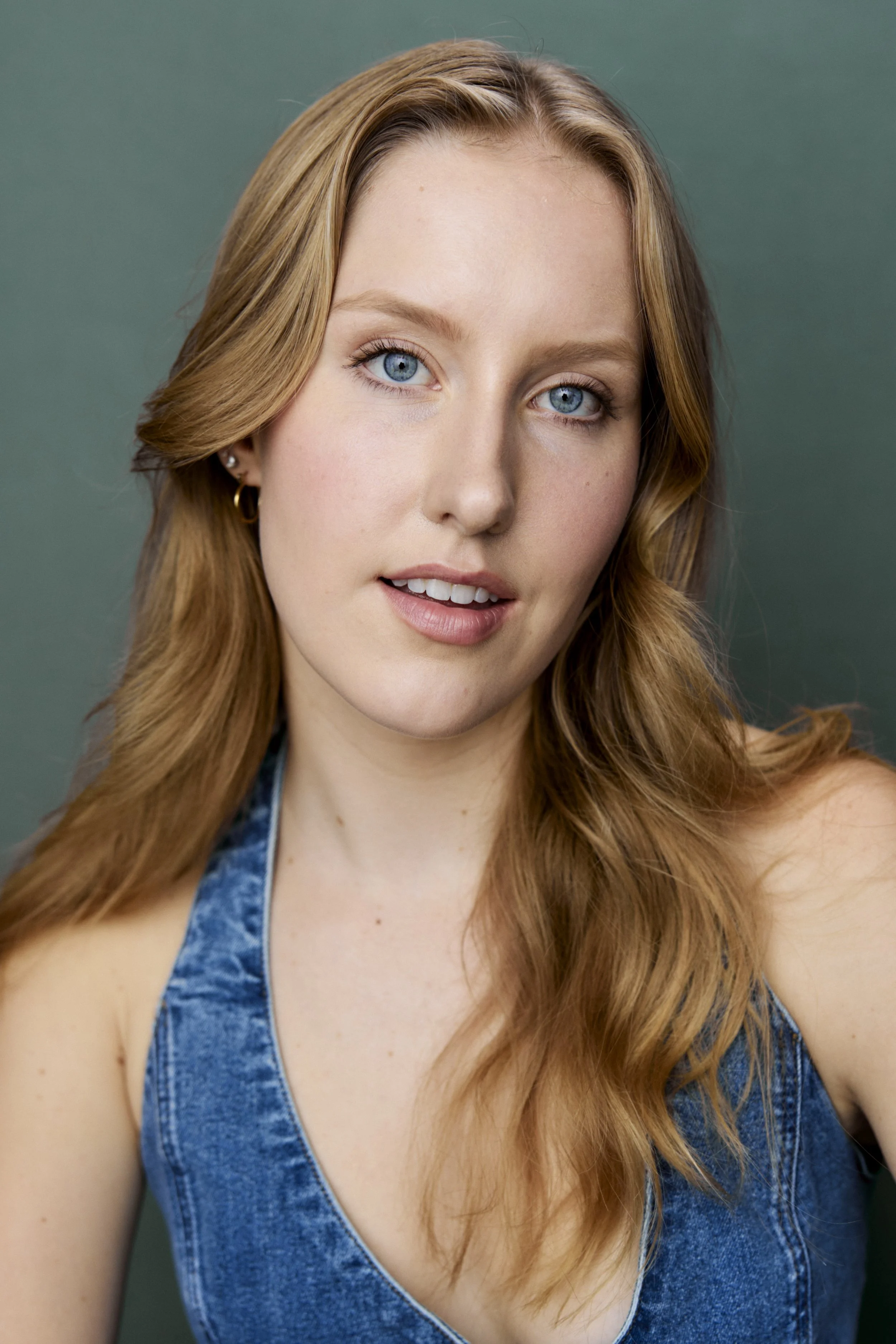 Mimi Pietila, a young actress with blonde hair and blue eyes in a denim top against a turquoise backdrop