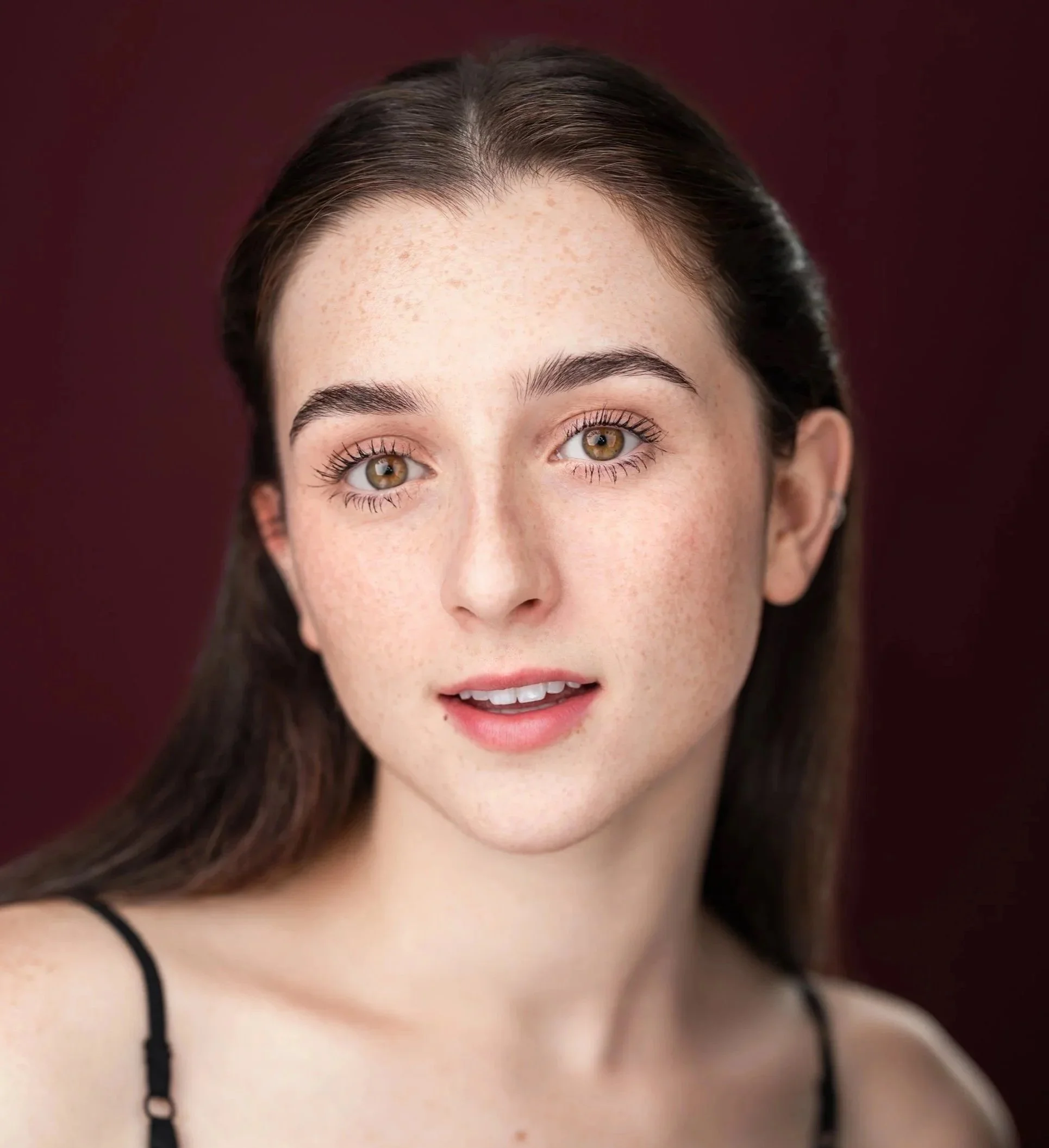 Close-up of Gemma Strauss, a young actress, highlighting her eyes, eyebrows, and upper cheeks with a dark red background.