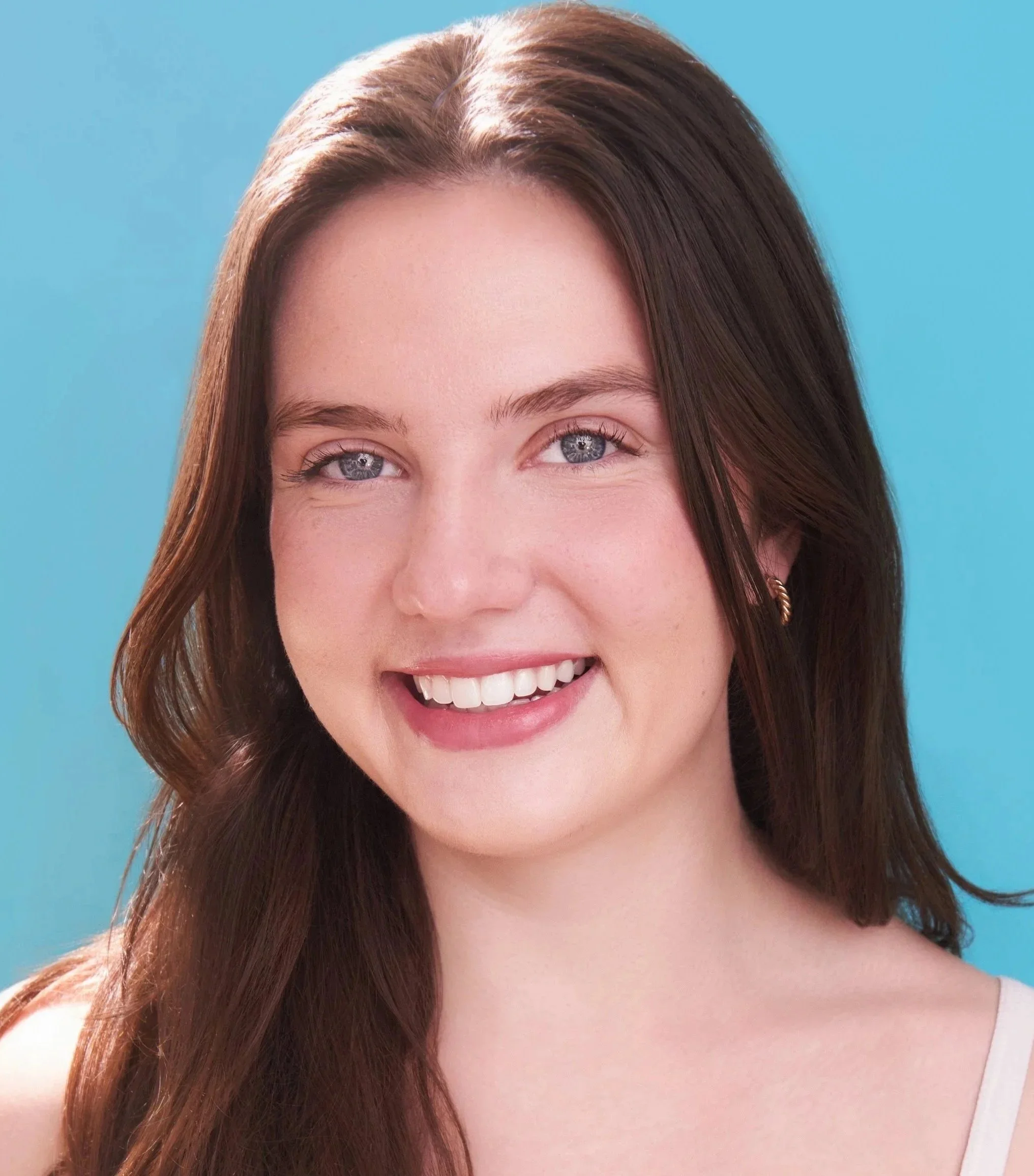 Close-up of Elena Schlax, a young actress with blue eyes and long brown hair, against a blue background.