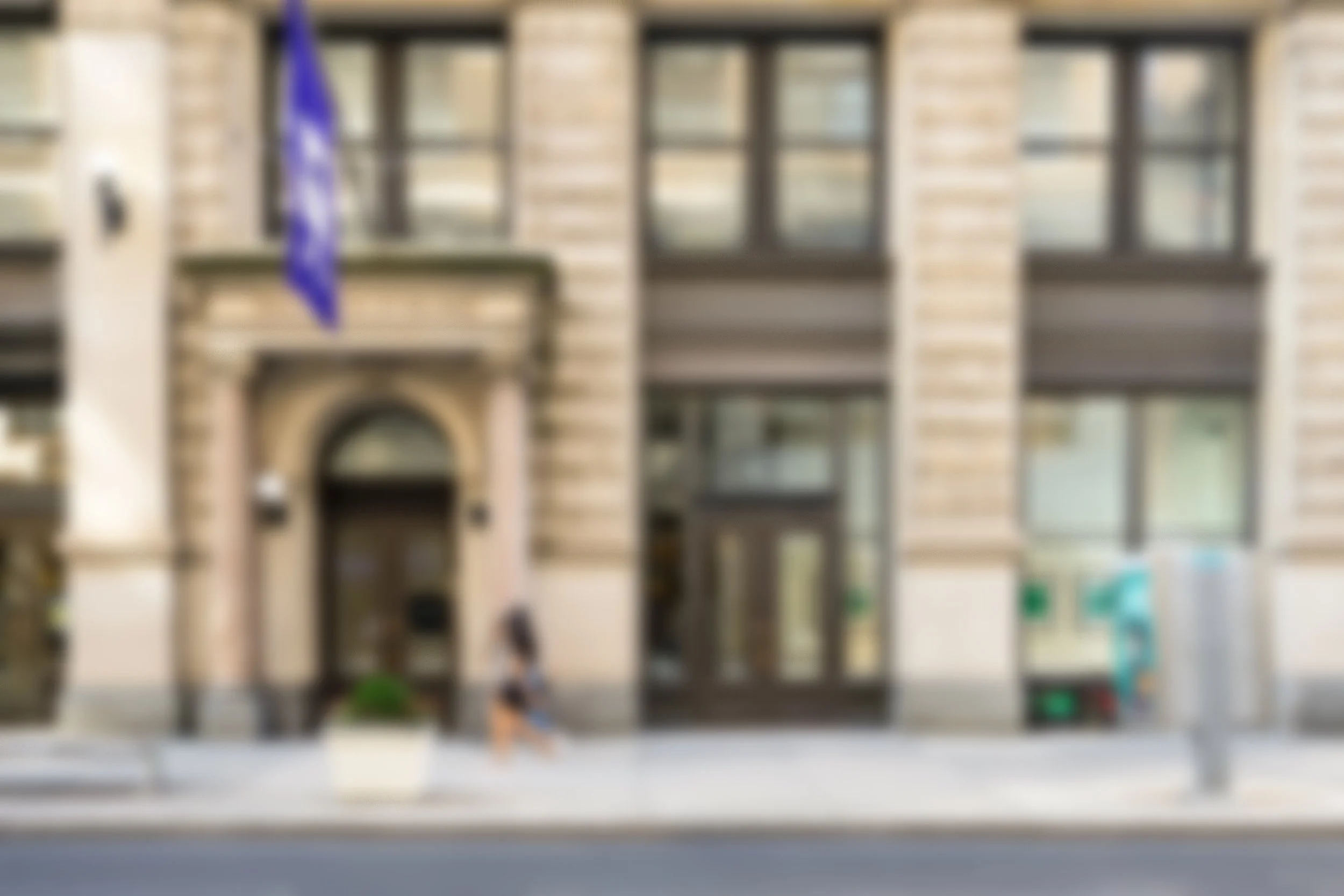 Blurred image of NYU Tisch School of the Arts, a tan building with the NYU flag hanging above the door.