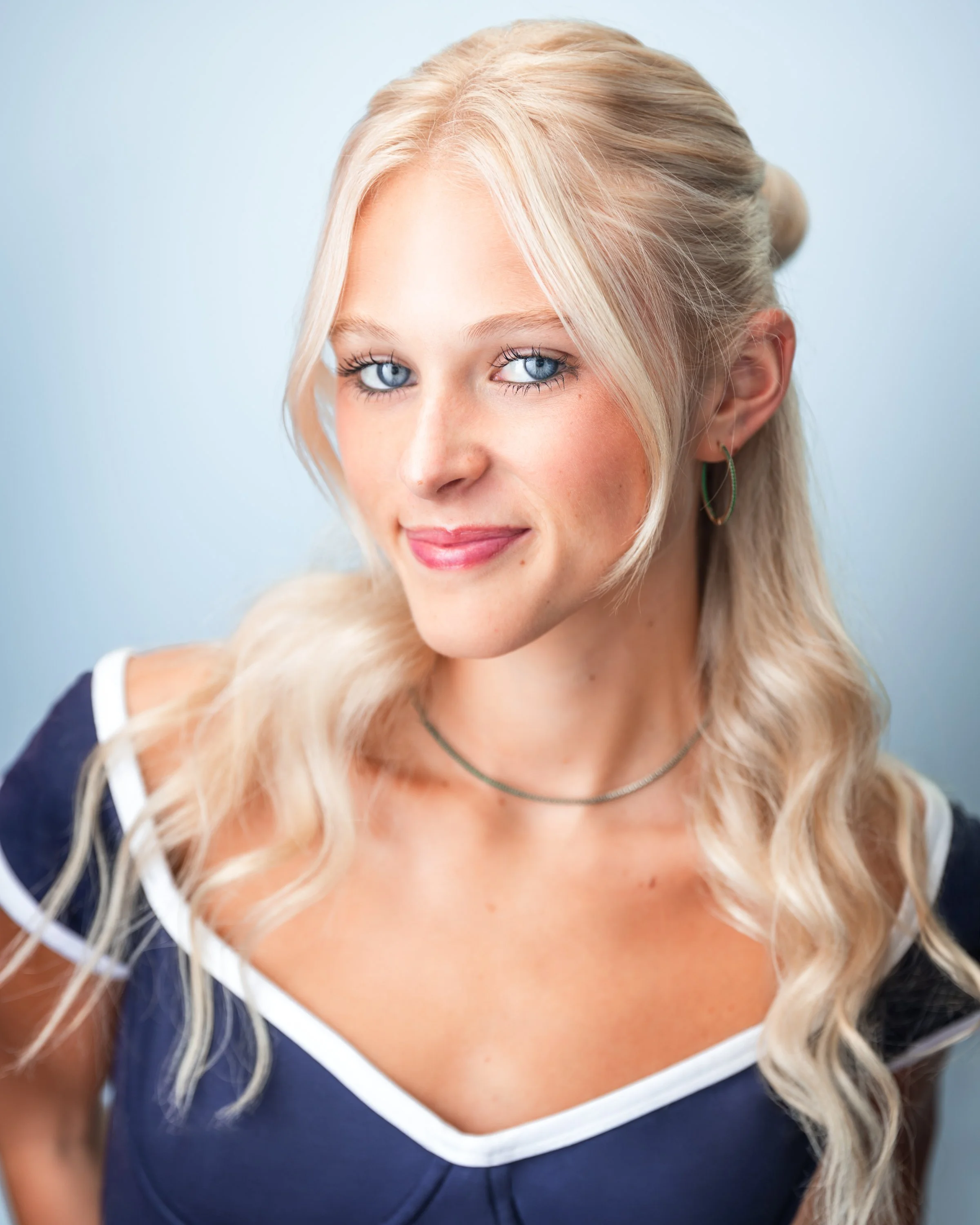 Mia Goldammer, a young actress with light blonde hair and blue eyes, in a navy and white top against a light blue backdrop