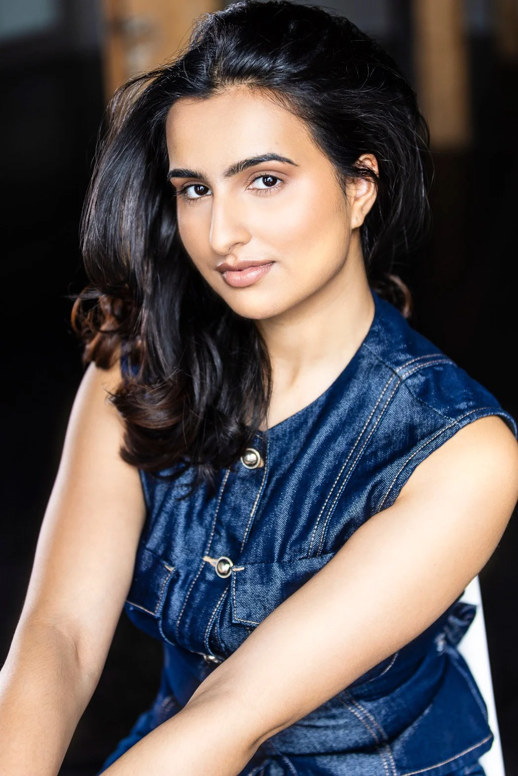 Portrait of Uma Bains, a young woman with dark, wavy hair, wearing a sleeveless denim top, looking at the camera with a slight smile.