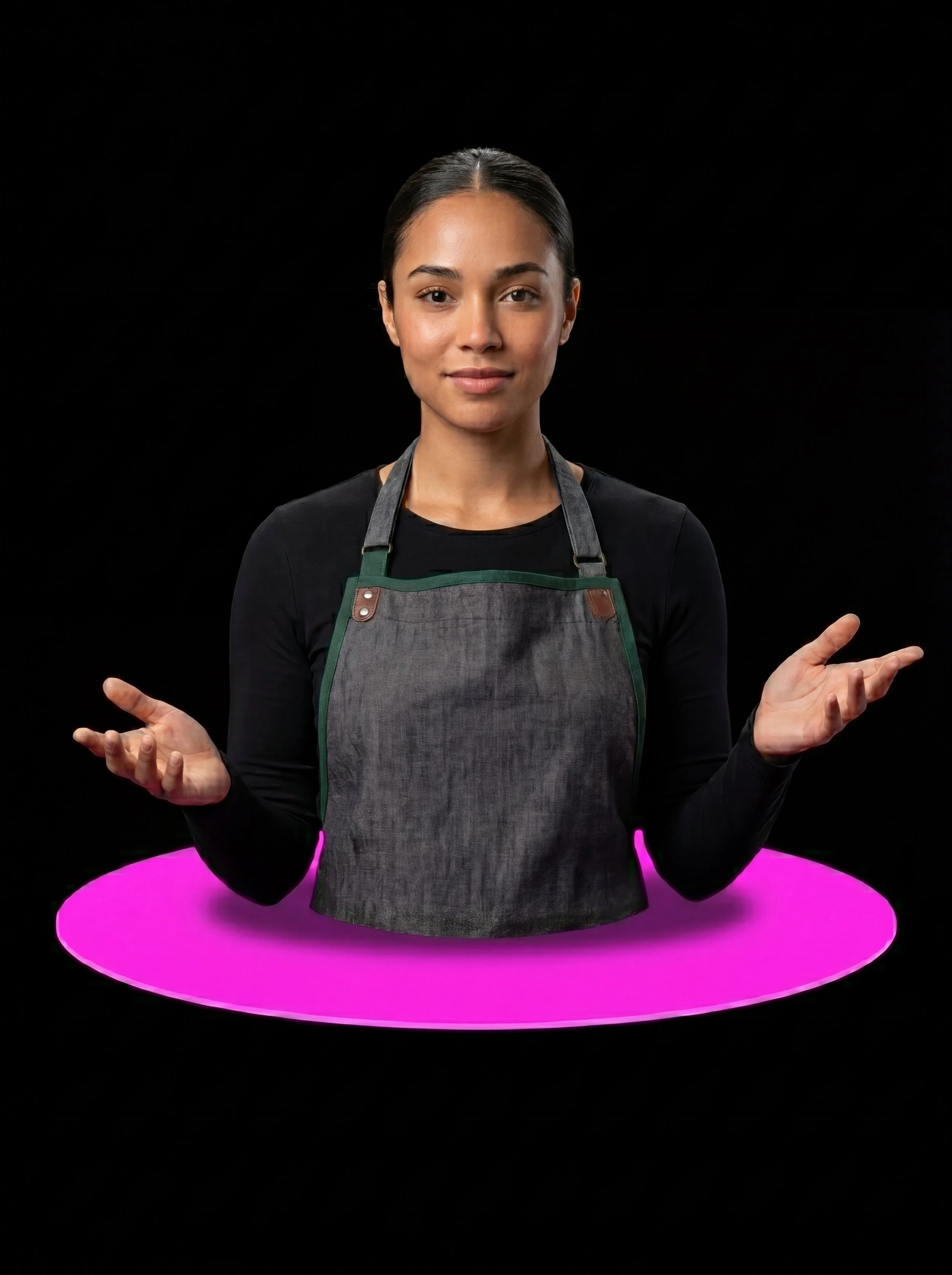 A woman with dark hair in a bun, wearing a black shirt and a grey apron, standing in front of a black background with a pink glowing ring at her waist, gesturing with her hands.