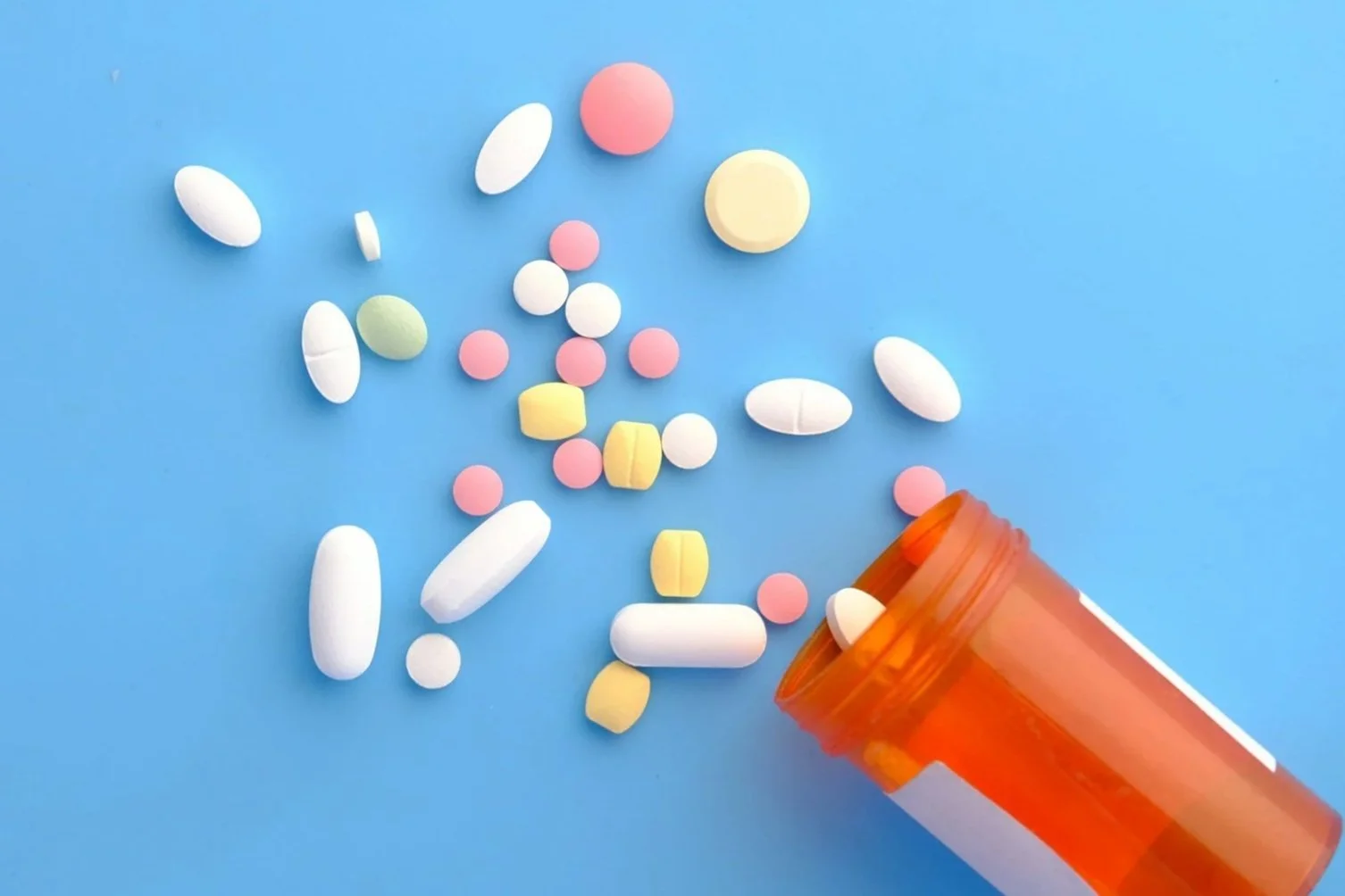 Assorted pills and tablets spilling out of an orange prescription bottle onto a blue surface.