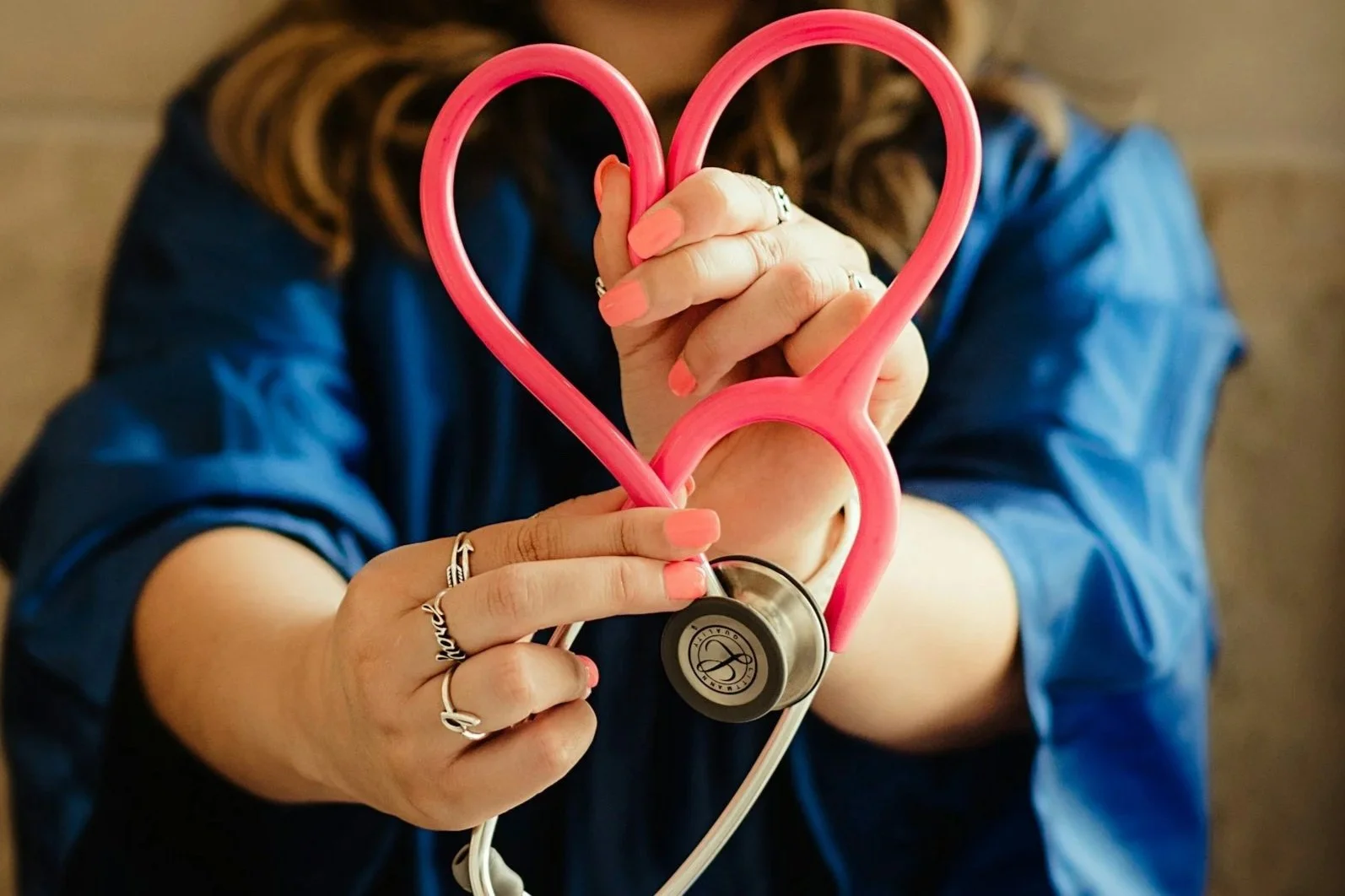 Person wearing a blue shirt holding a pink heart-shaped stethoscope