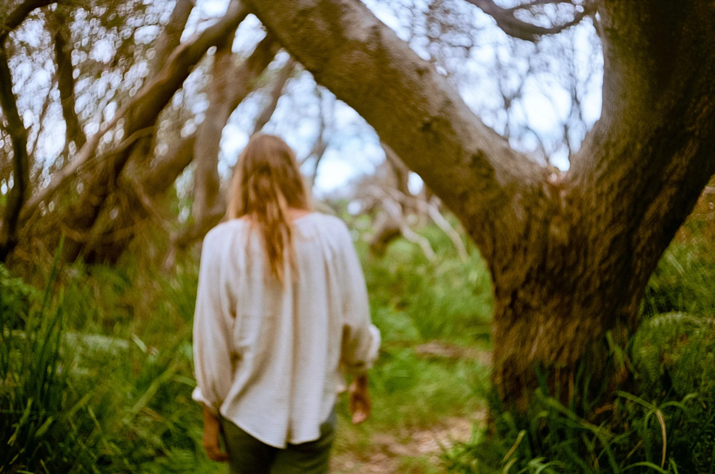 Lauren walking away from camera through coastal scrub, white linen on Yuin Country NSW
