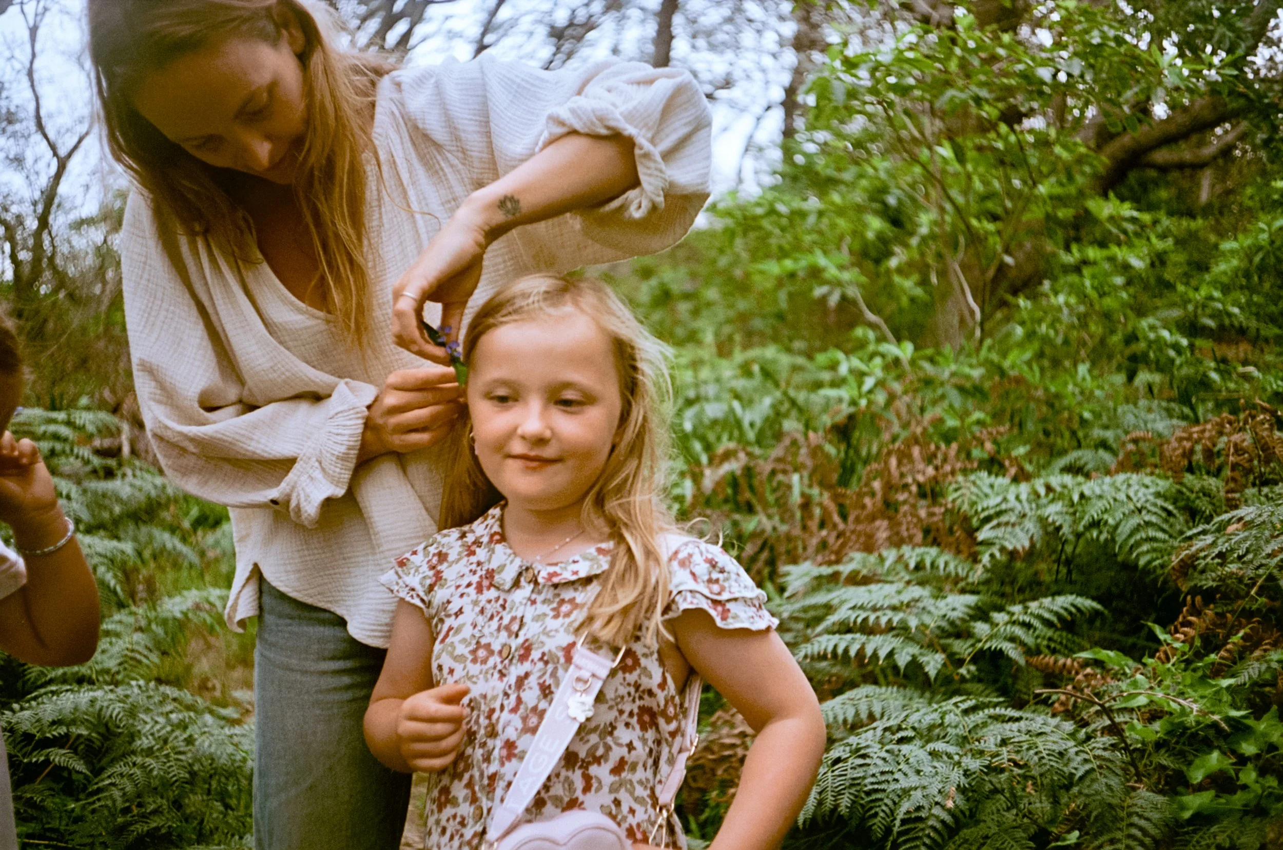 Lauren placing a flower in her daughter's hair amid coastal ferns on Yuin Country, NSW.
