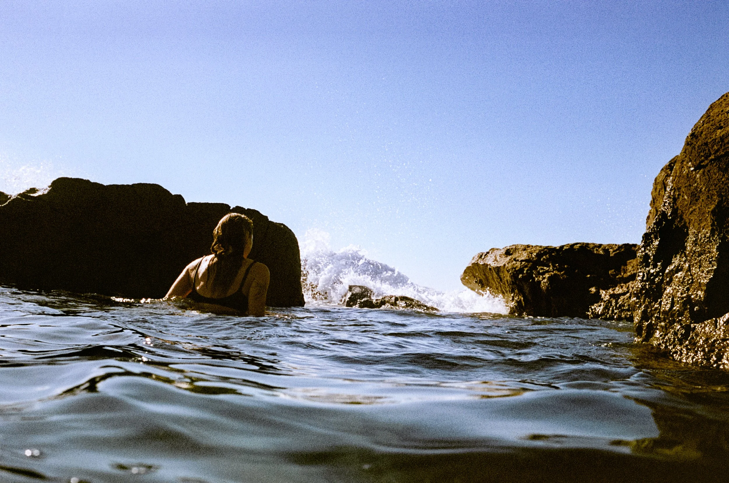 Lauren in the water, back to camera, heading towards coastal rocks on the NSW South Coast.