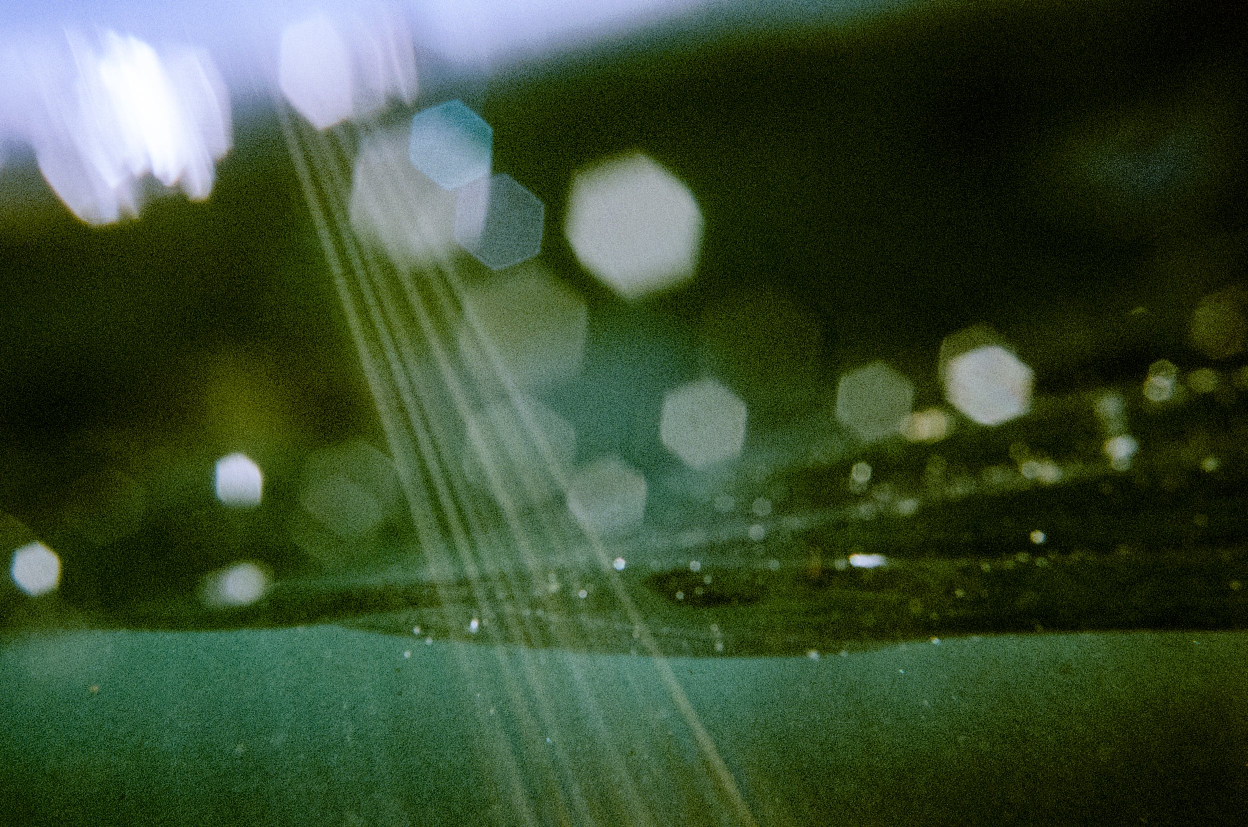 Abstract bokeh, lens flares through dark green ocean.  Yuin Country, NSW.