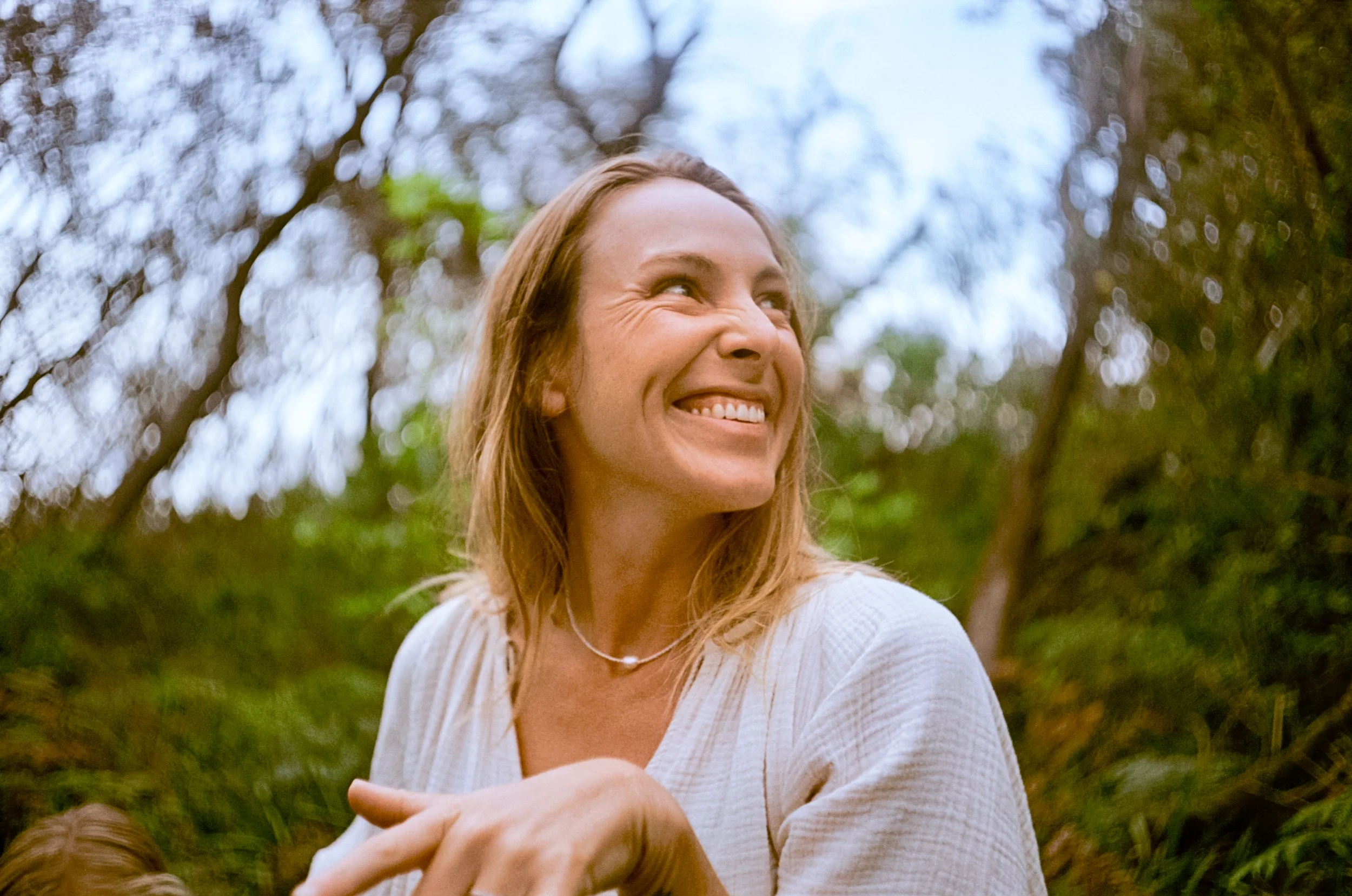 ounder portrait close-up, laughing, dappled bush light. > Lauren Ramisch — somatic mentor on Yuin Country, NSW.