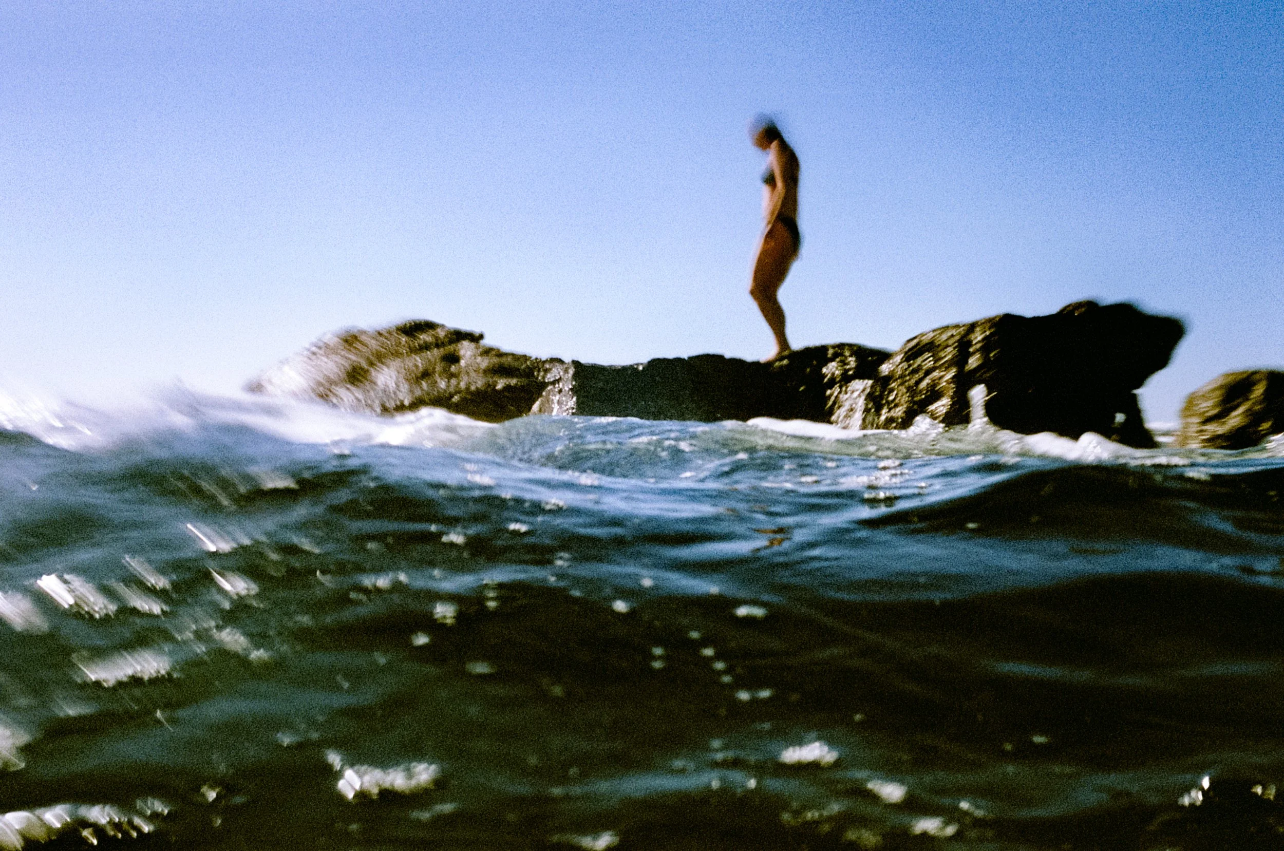 Lauren silhouetted on coastal rocks above the ocean, motion-blurred sea in the foreground, NSW South Coast.