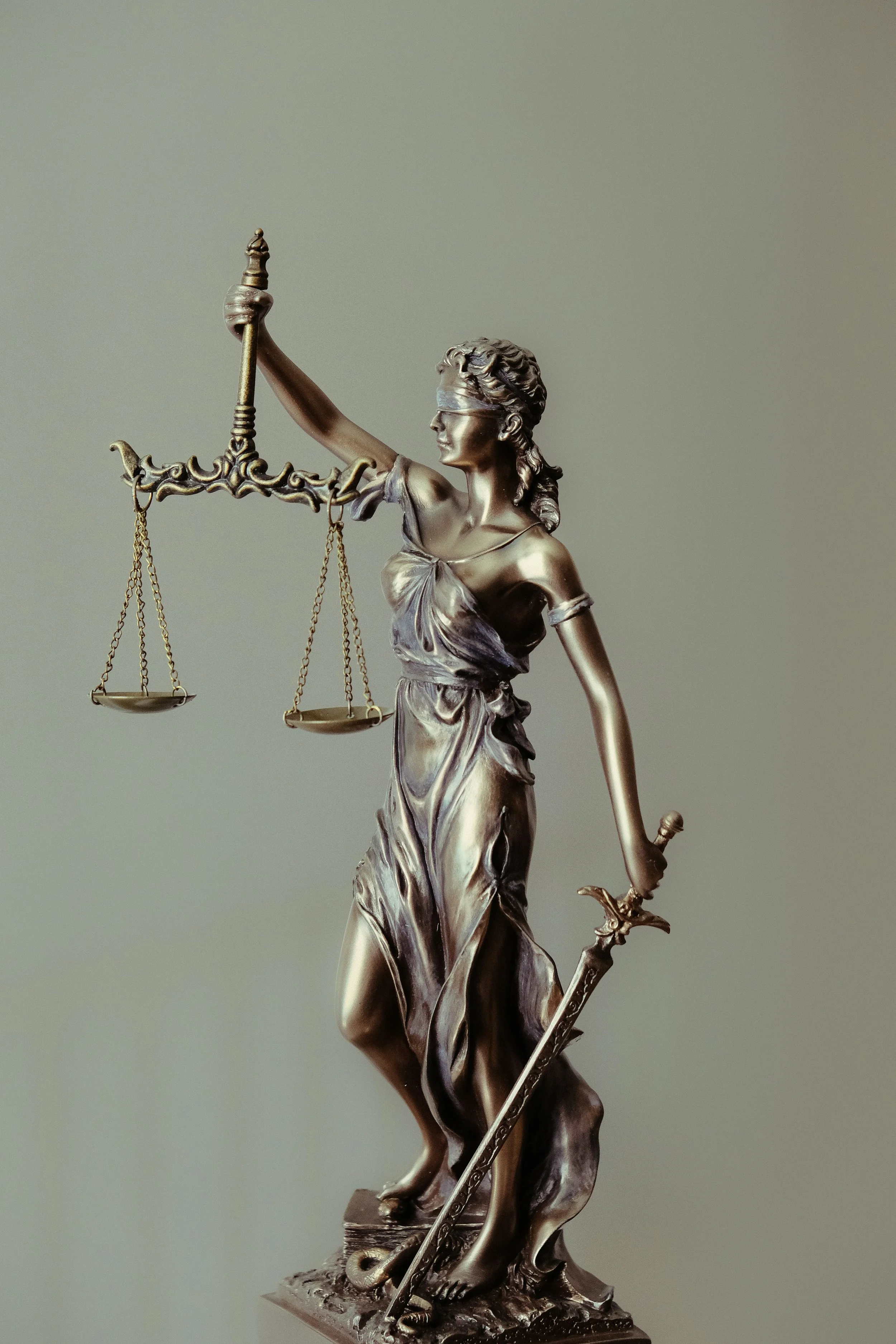 Bronze sculpture of Lady Justice holding scales in her left hand and a sword in her right hand, wearing a blindfold, and standing on a decorated base.