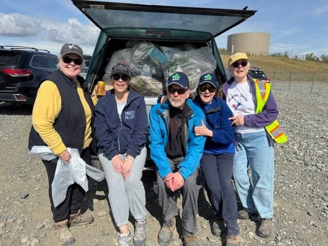 Five people standing in front of an open hatchback filled with bags and supplies during daytime outdoor event, some wearing hats, sunglasses, and casual clothing.