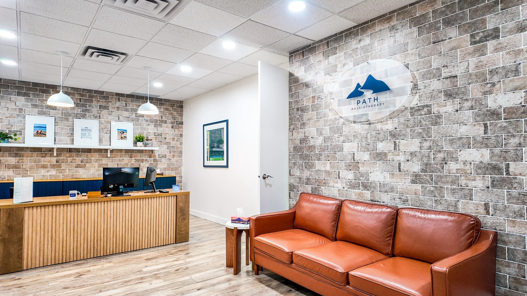 Path Physiotherapy reception area with wood desk, brick accent walls, and brown leather sofa