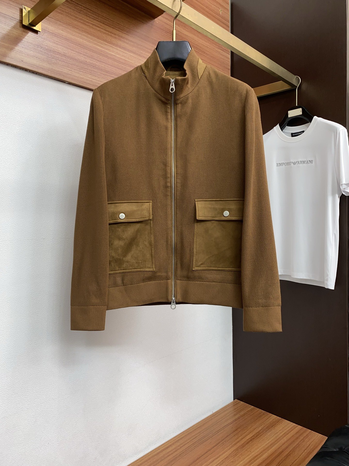 Brown zip-up jacket with large front pockets hanging on a black hanger in a retail store.