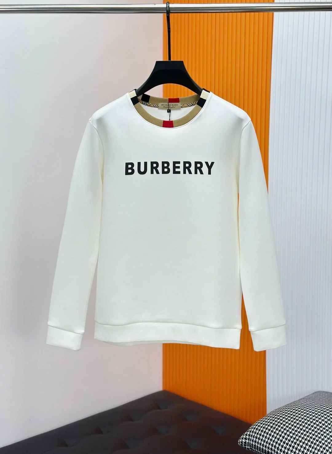 White sweatshirt with 'BURBERRY' printed on front, hanging on a black hanger in a retail store