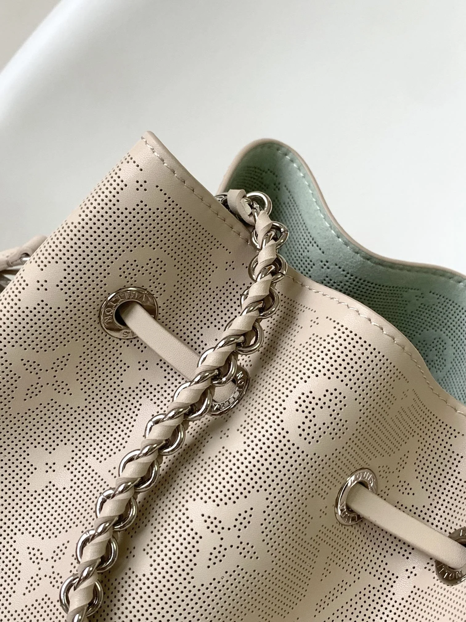 Close-up of a designer handbag with a perforated pattern, silver chain strap, and eyelet closures.