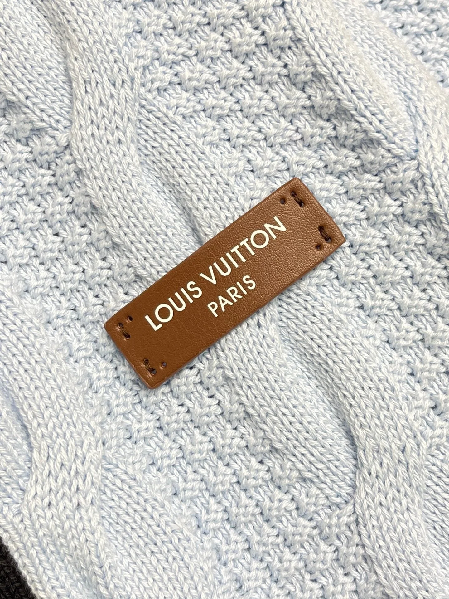 Close-up of a white knitted fabric with a brown leather tag that reads 'LOUIS VUITTON PARIS'.