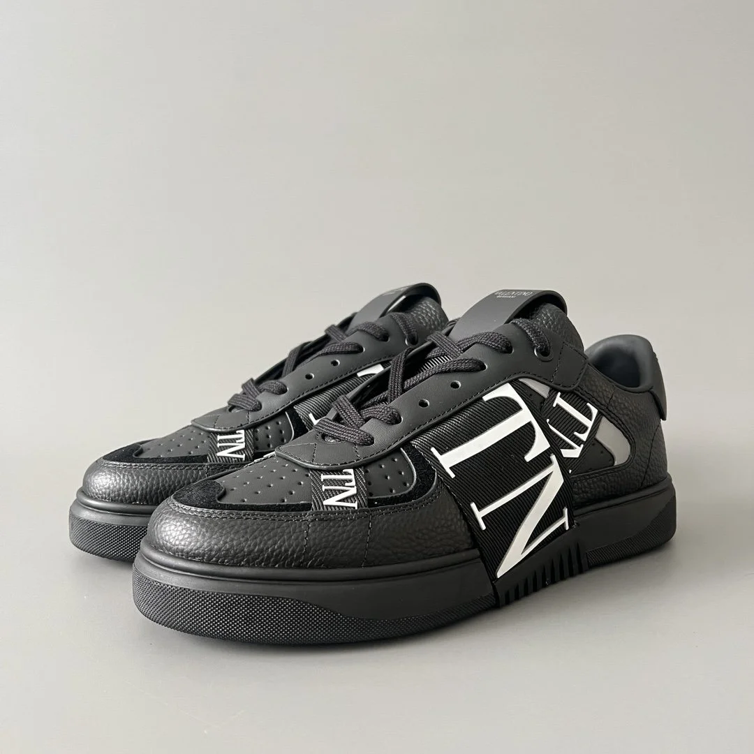 Black designer sneakers with bold white lettering and textured details on a plain surface.