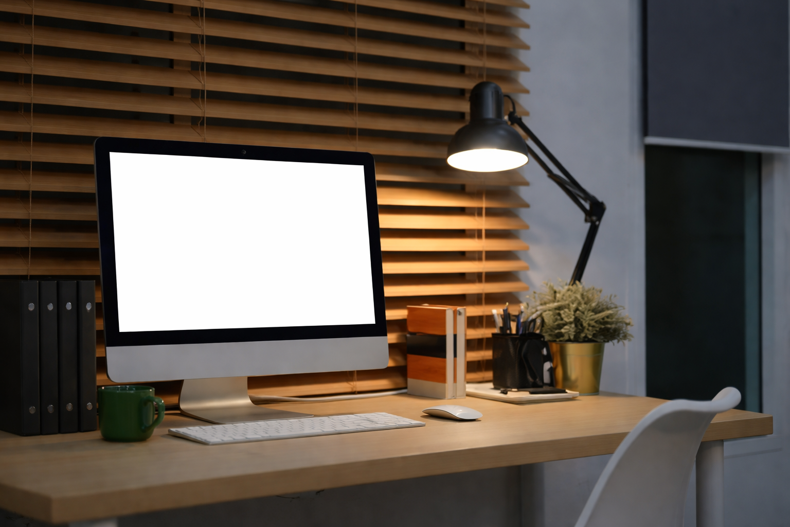 Home office desk with an iMac computer, a green mug, a row of black binders, a white keyboard and mouse, a desk lamp, and a plant in a gold pot, with wooden slats on the wall in the background.