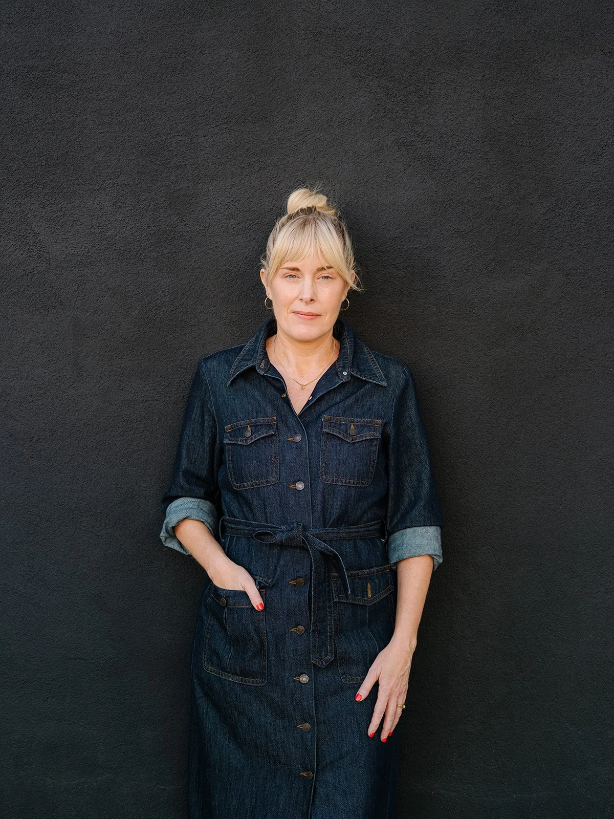 Jenny Walters, LMFT, depth psychotherapist in Los Angeles, standing in a denim dress against a dark textured wall