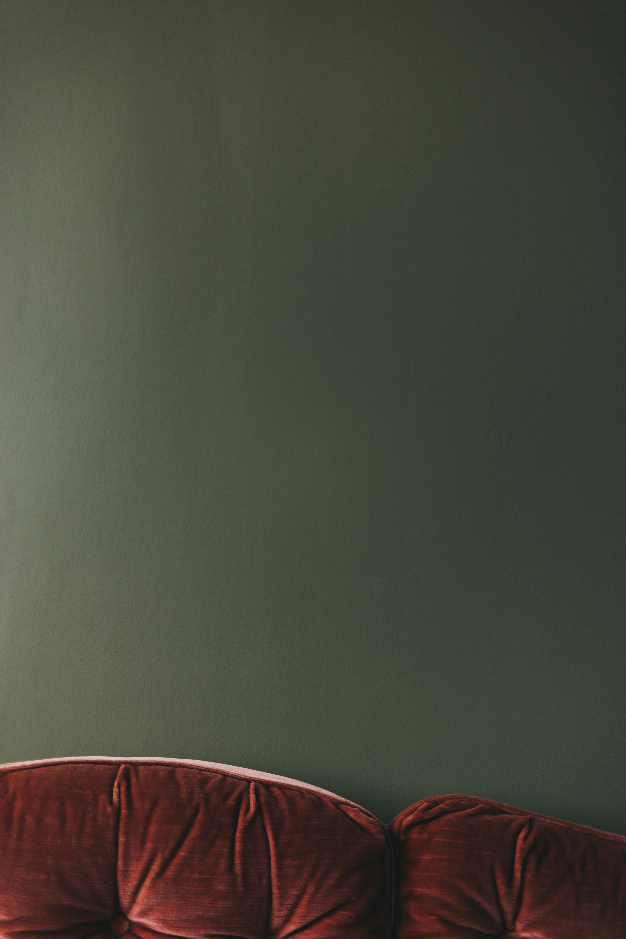 A section of a brown velvet sofa against a dark green painted wall.