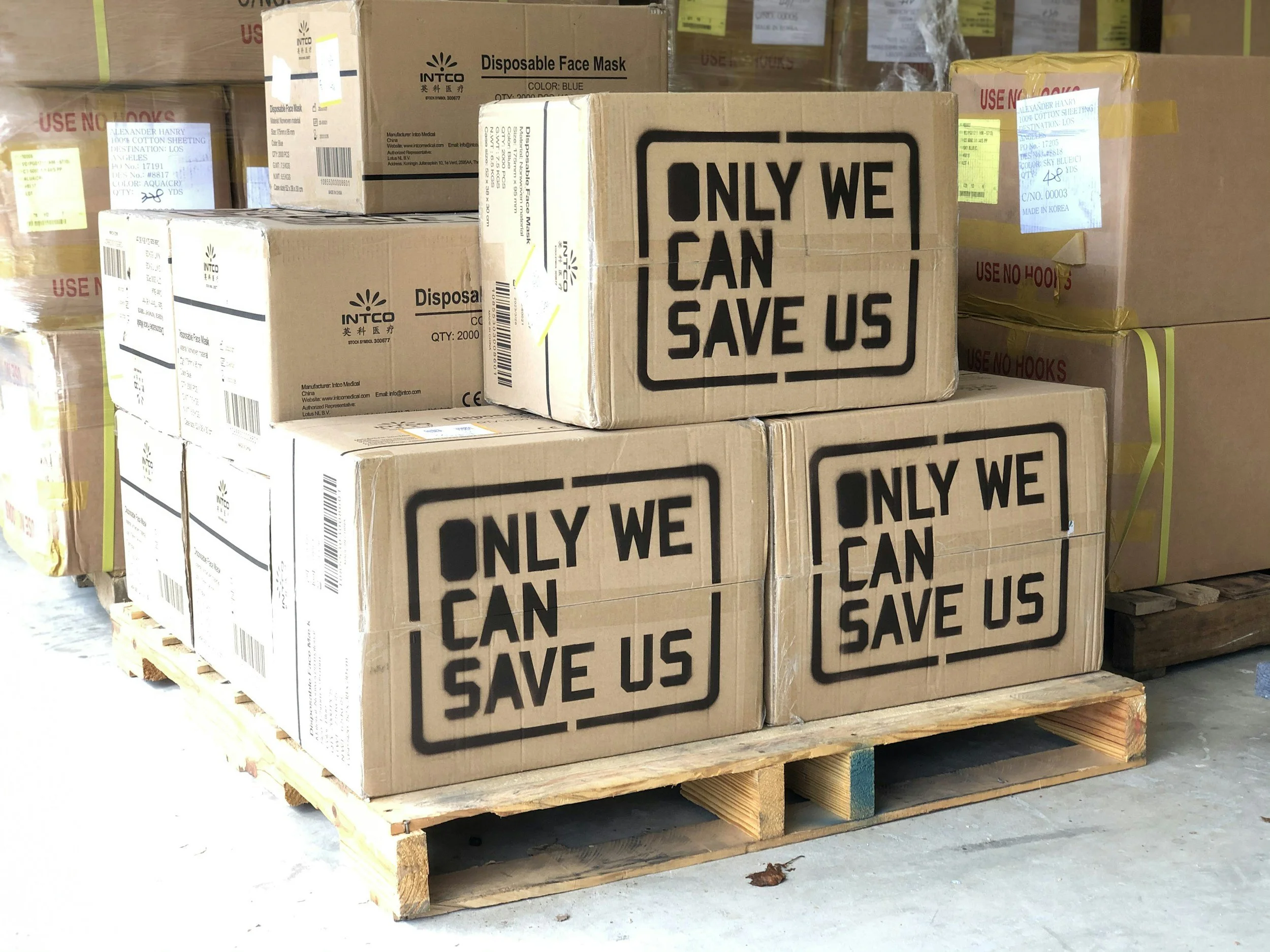 Stack of cardboard boxes on a wooden pallet labeled with the message 'ONLY WE CAN SAVE US.'