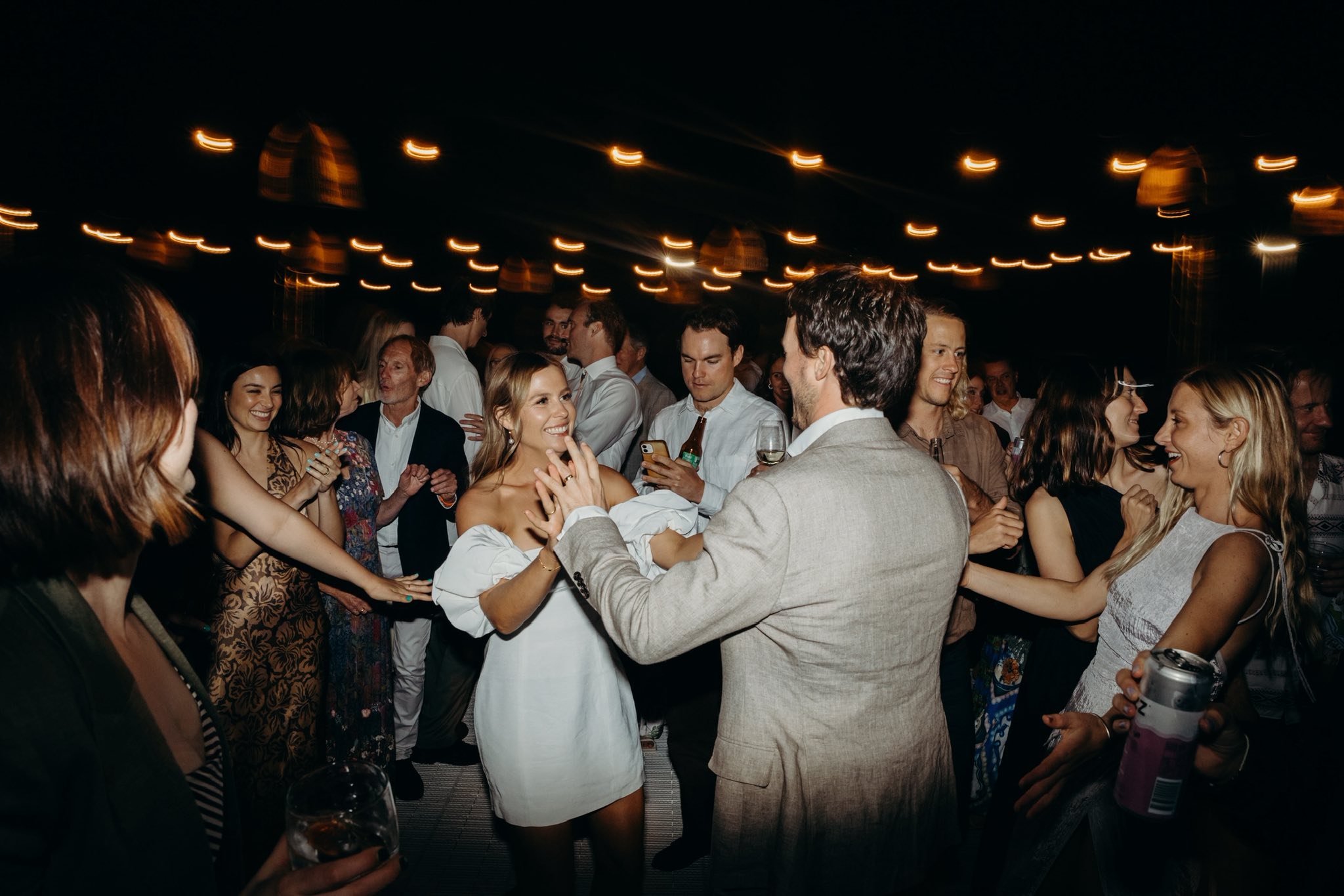 People dancing and socializing at a party under string lights at night.
