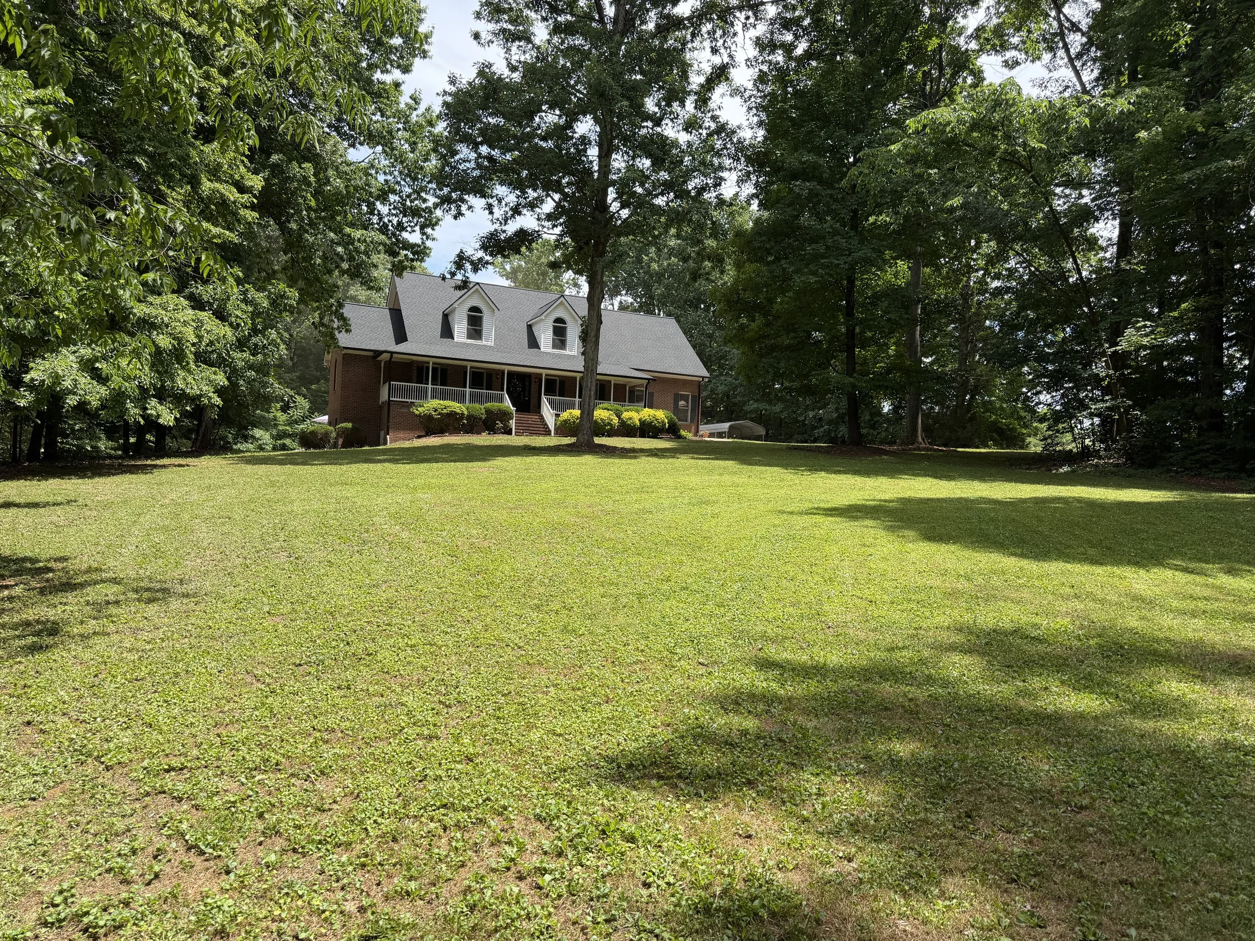 A house with a grey roof and brick exterior, surrounded by trees and a well-maintained lawn.