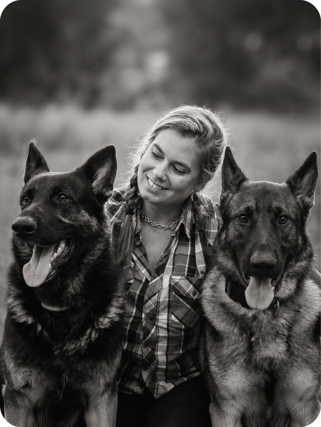 A woman smiling with two German Shepherd dogs outdoors in black and white.