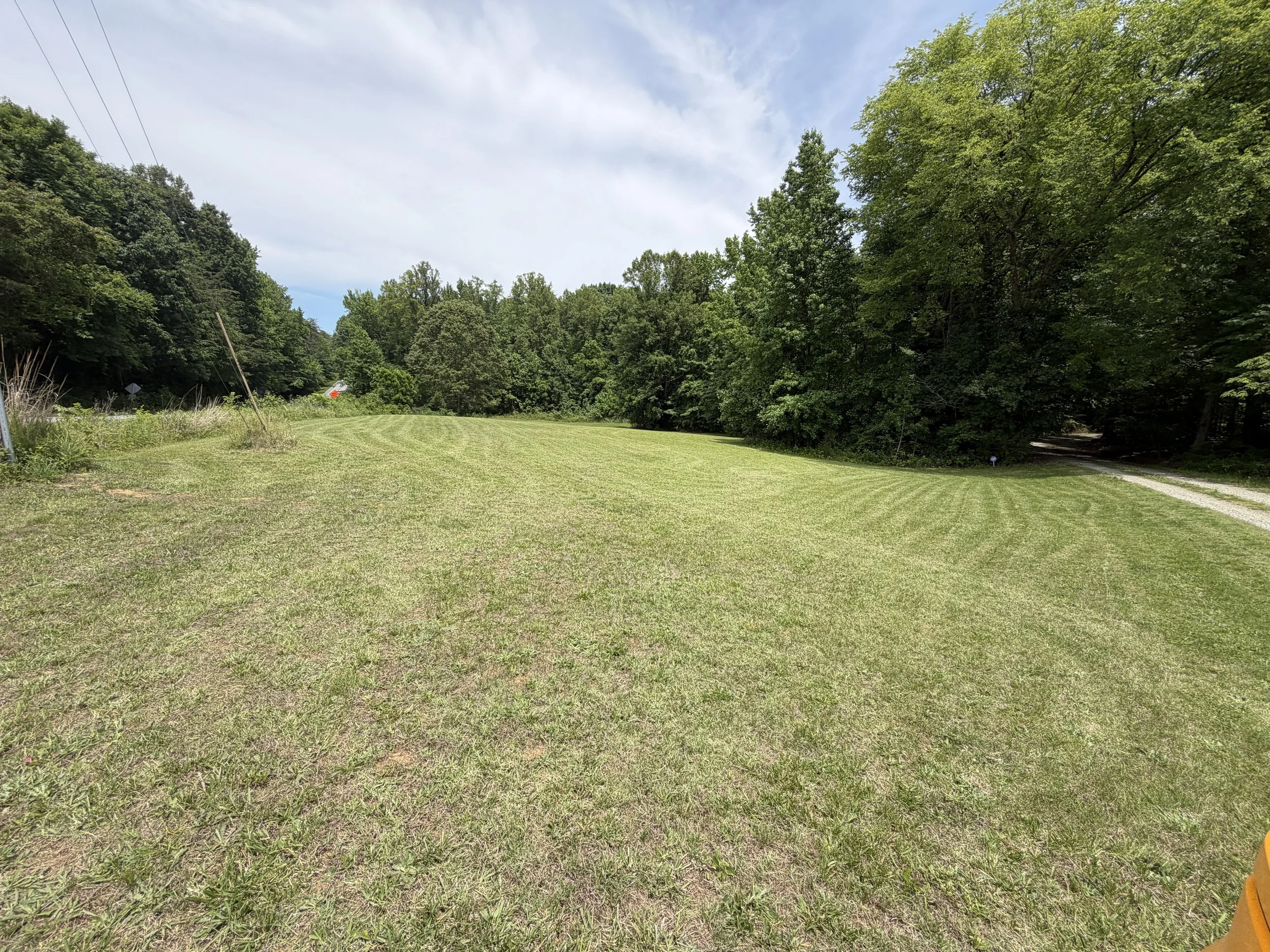 A grassy clearing bordered by dense trees on both sides under a partly cloudy sky.