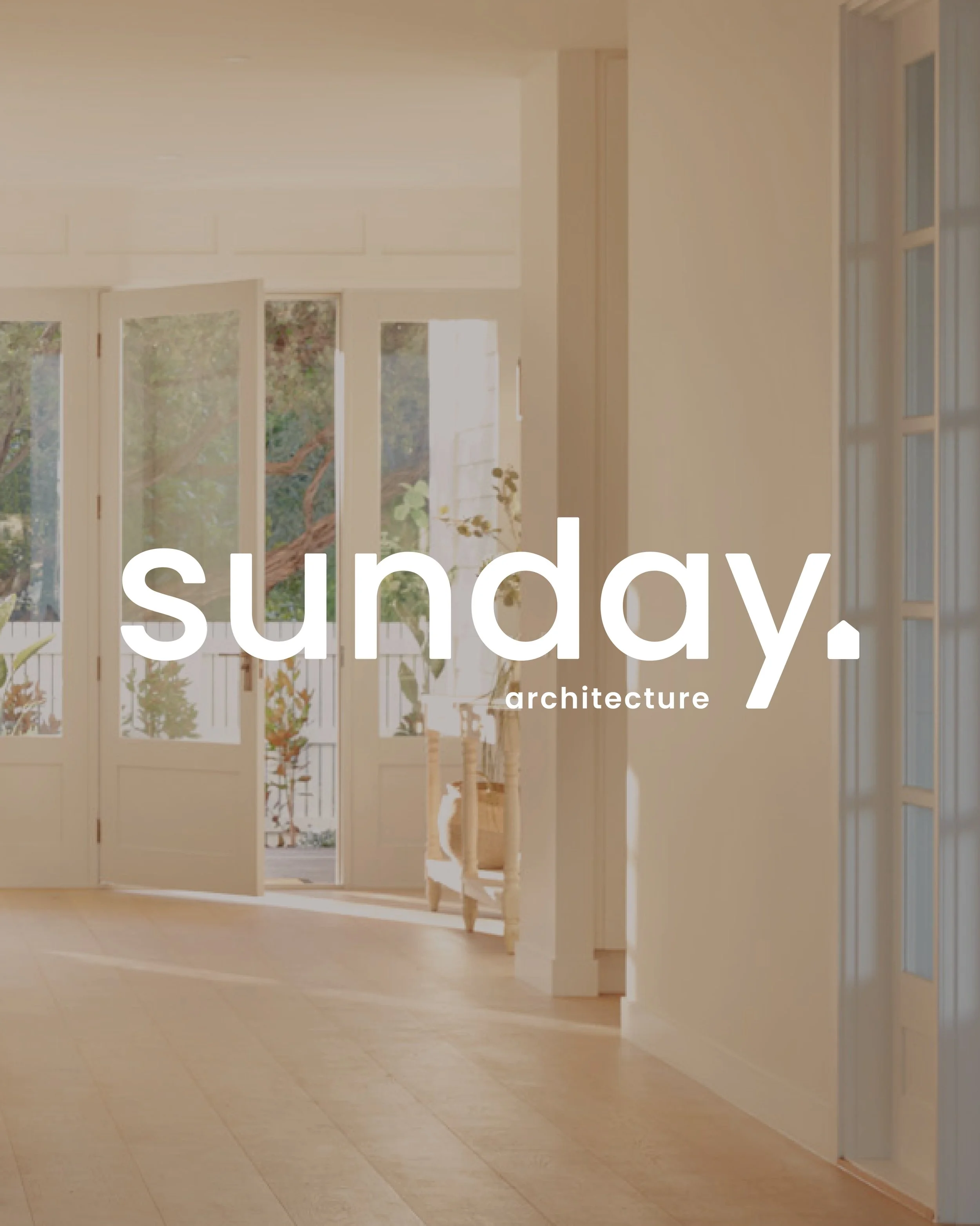 Wide view of a bright, spacious interior with open double doors leading to a patio, featuring sunlight streaming in, with the words "sunday. architecture" overlaid.