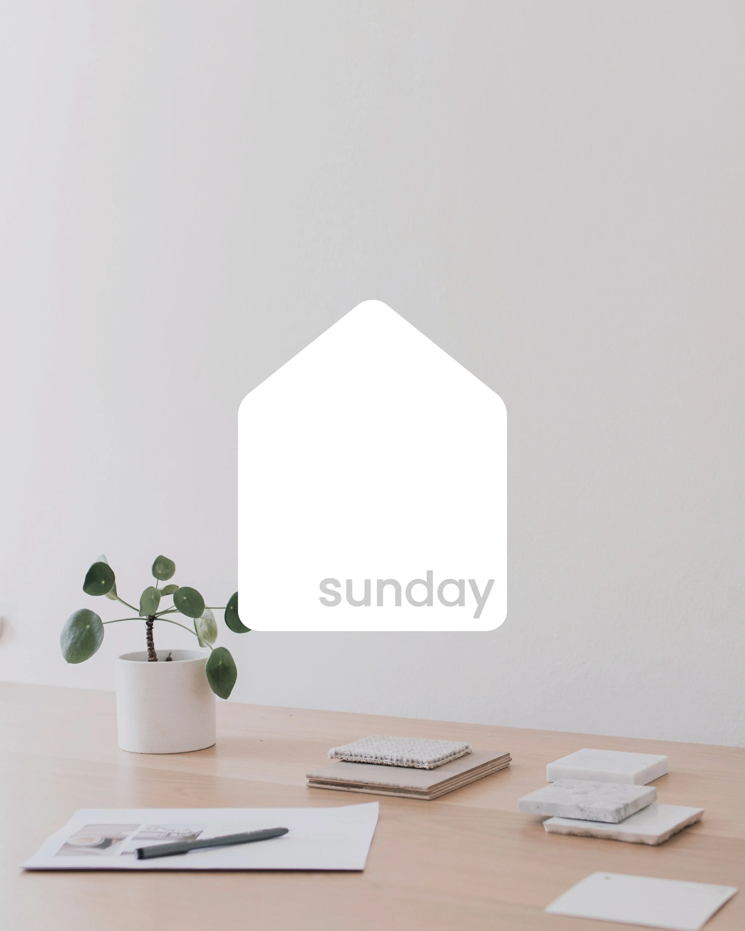 Minimalist workspace with a small plant, coasters, paper, and a pen on a light wood desk. "Sunday" text in a house-shaped design overlay.