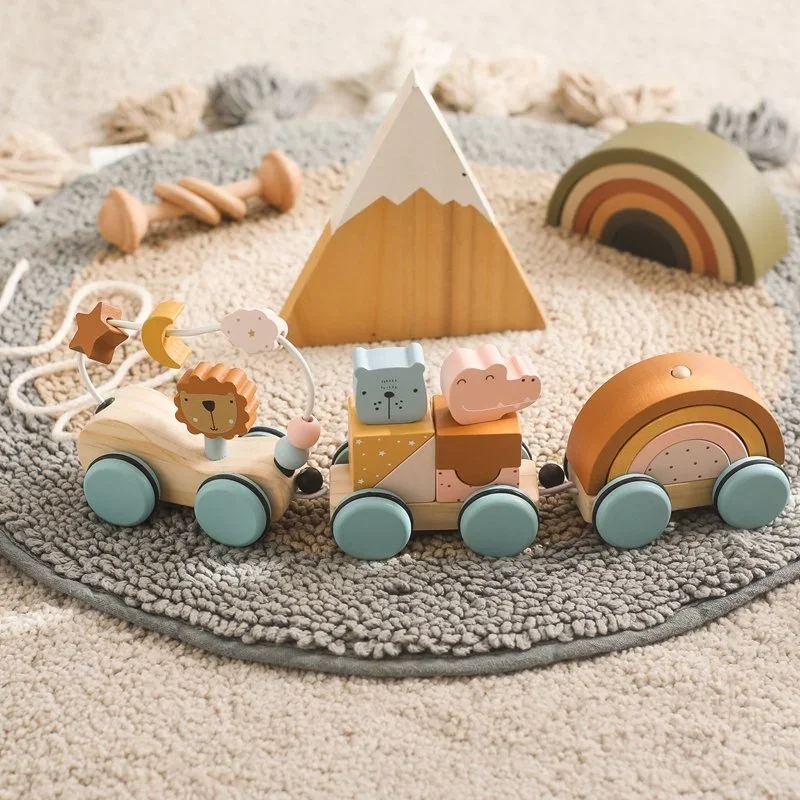Wooden toy train with animal faces on each car, placed on a round textured rug with a wooden mountain decoration and a rainbow-shaped piece in the background.