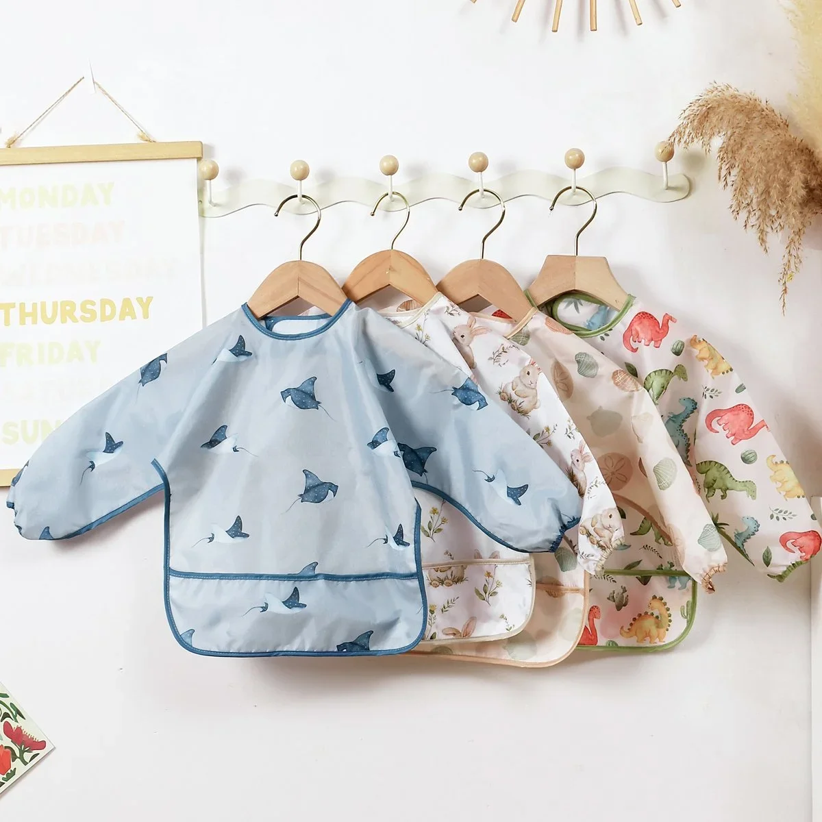 Children's rain ponchos with colorful animal patterns hanging on hooks in a room.