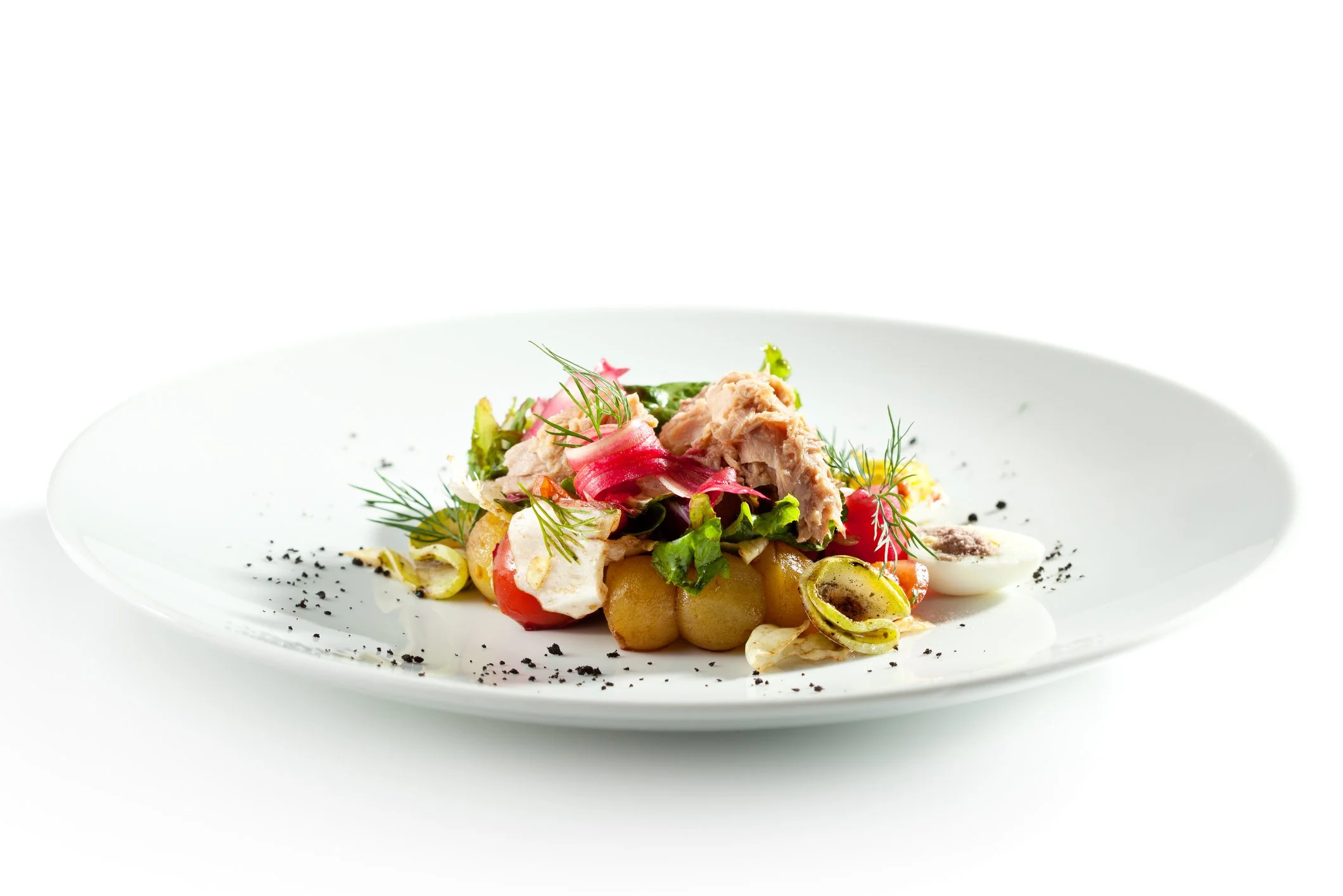 Elegant plated dish featuring chickpeas, tuna, pickled vegetables, herbs, and garnishes on a white plate.