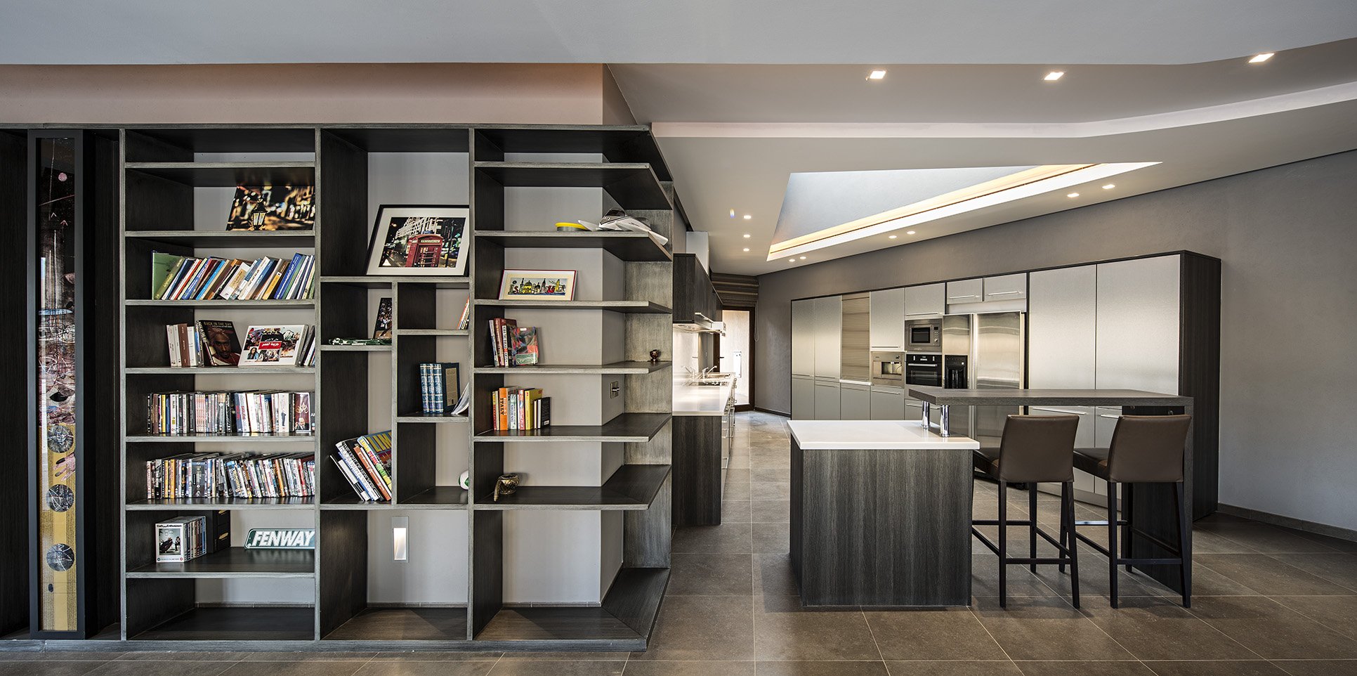 Modern open-concept kitchen with dark wood cabinetry, stainless steel appliances, white countertops, and a bar area with two dark leather barstools.