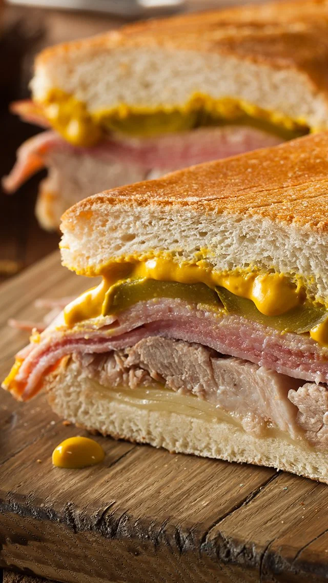 Close-up of a club sandwich on a wooden board, showing layers of turkey, bacon, pickles, mustard, and toasted bread.