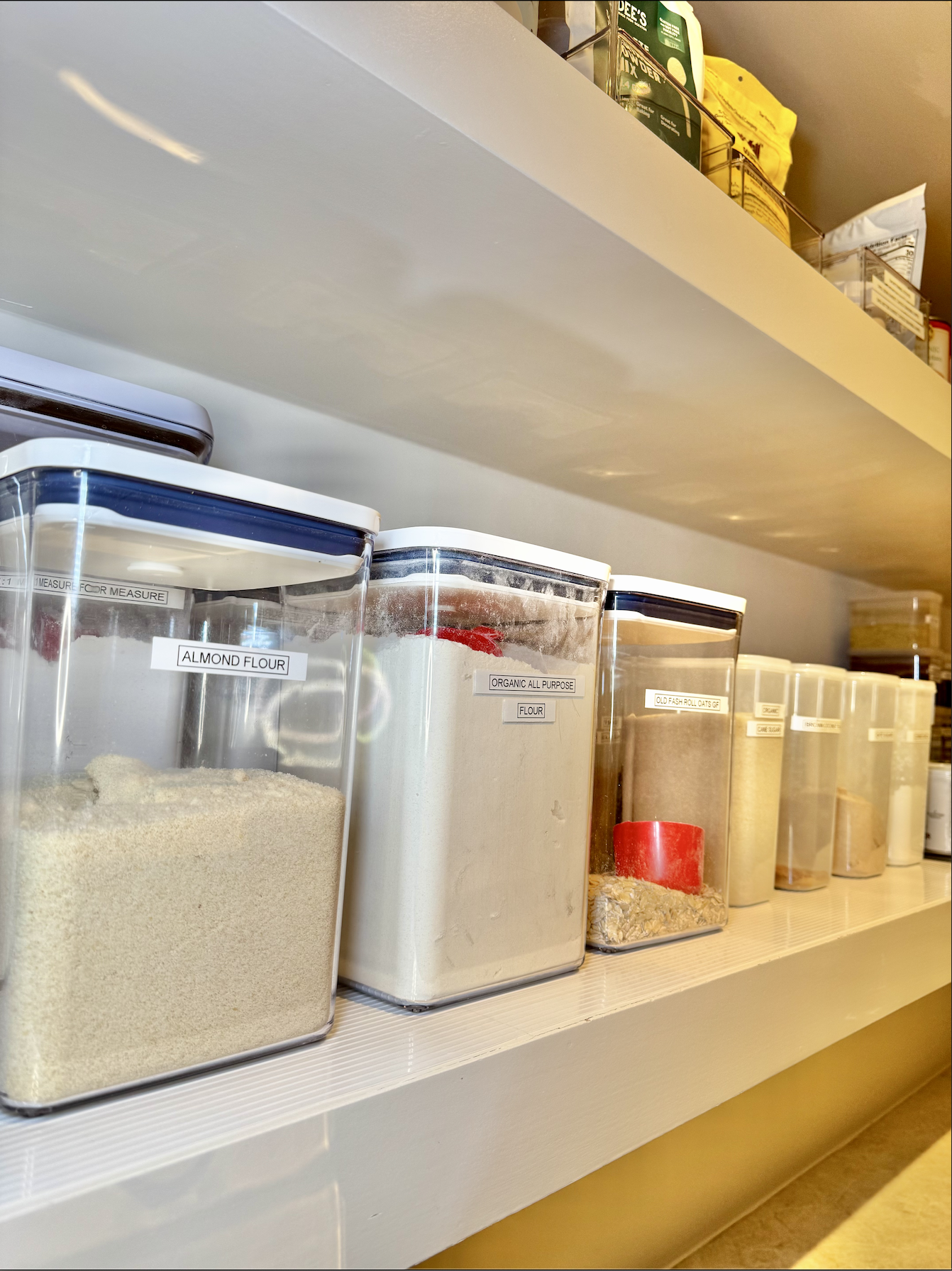 Kitchen pantry organizing; Clear plastic containers labeled for storing flour and oats, with pantry items visible on the top shelf - professional pantry organization by Ordered Living Co. Austin TX