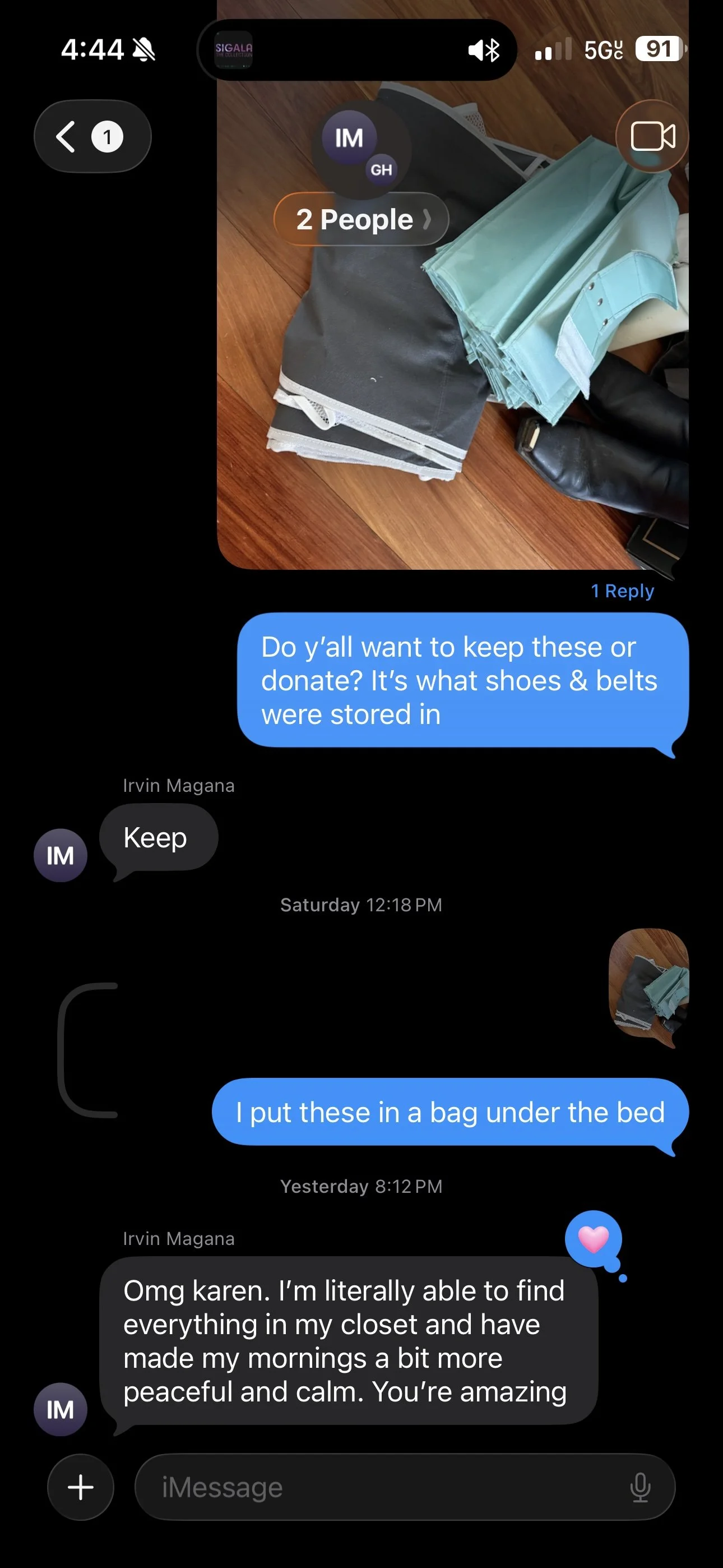 A smartphone screen showing a photo of neatly folded clothes, including black pants and light blue shirts, placed on a wooden surface.