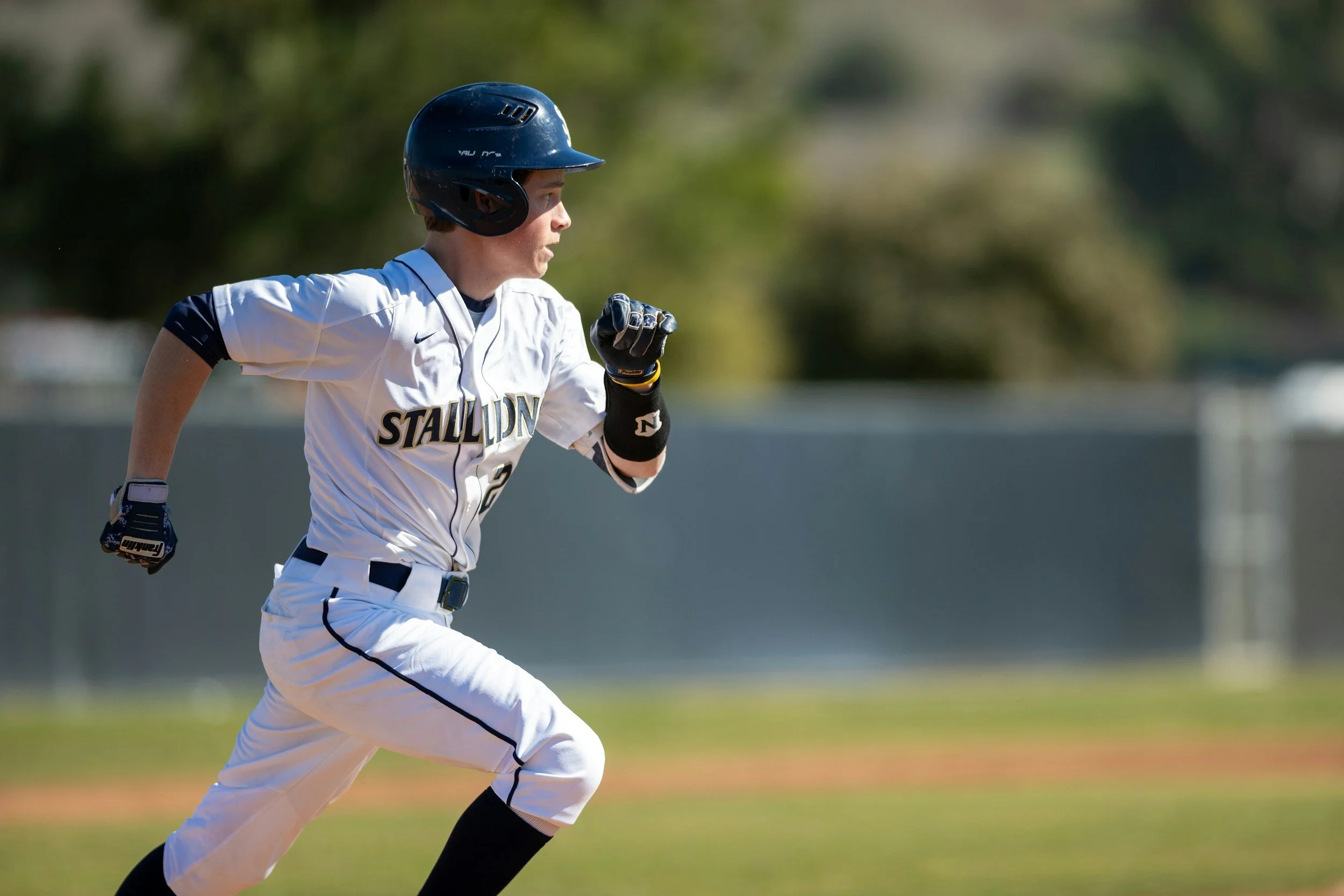 A young baseball player in a white uniform and black helmet running on a baseball field.