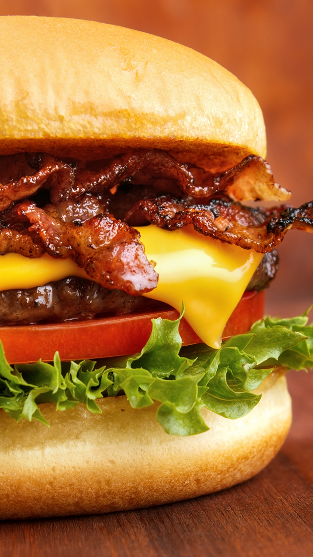 Close-up of a cheeseburger with bacon, cheese, tomato, lettuce, and a bun.