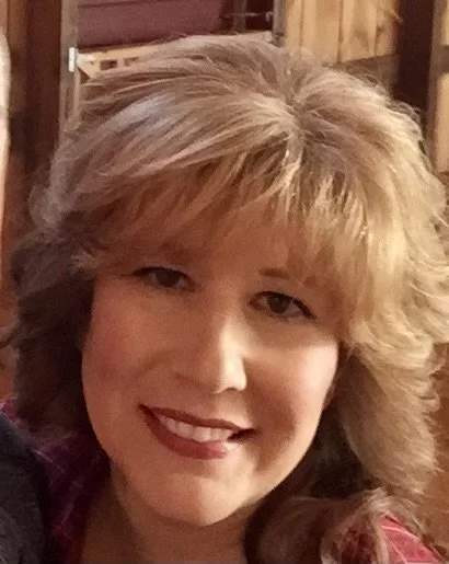Close-up of a woman smiling with blonde hair in a casual indoor setting.