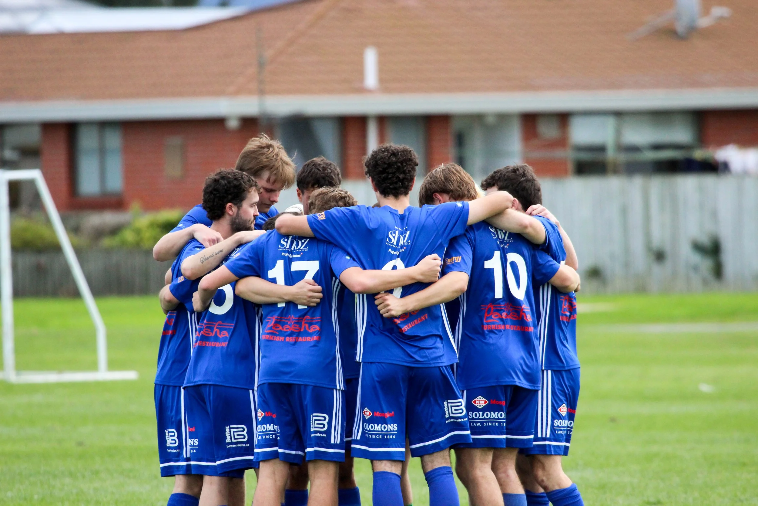 A group of soccer players in blue uniforms huddled together in a circle on a soccer field.
