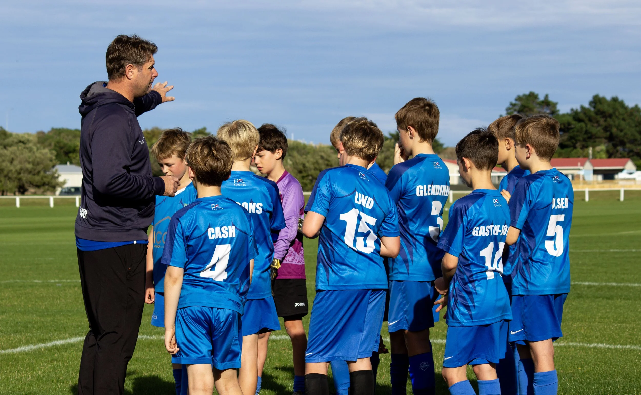 Young soccer players in blue uniforms listening to coach on a soccer field.