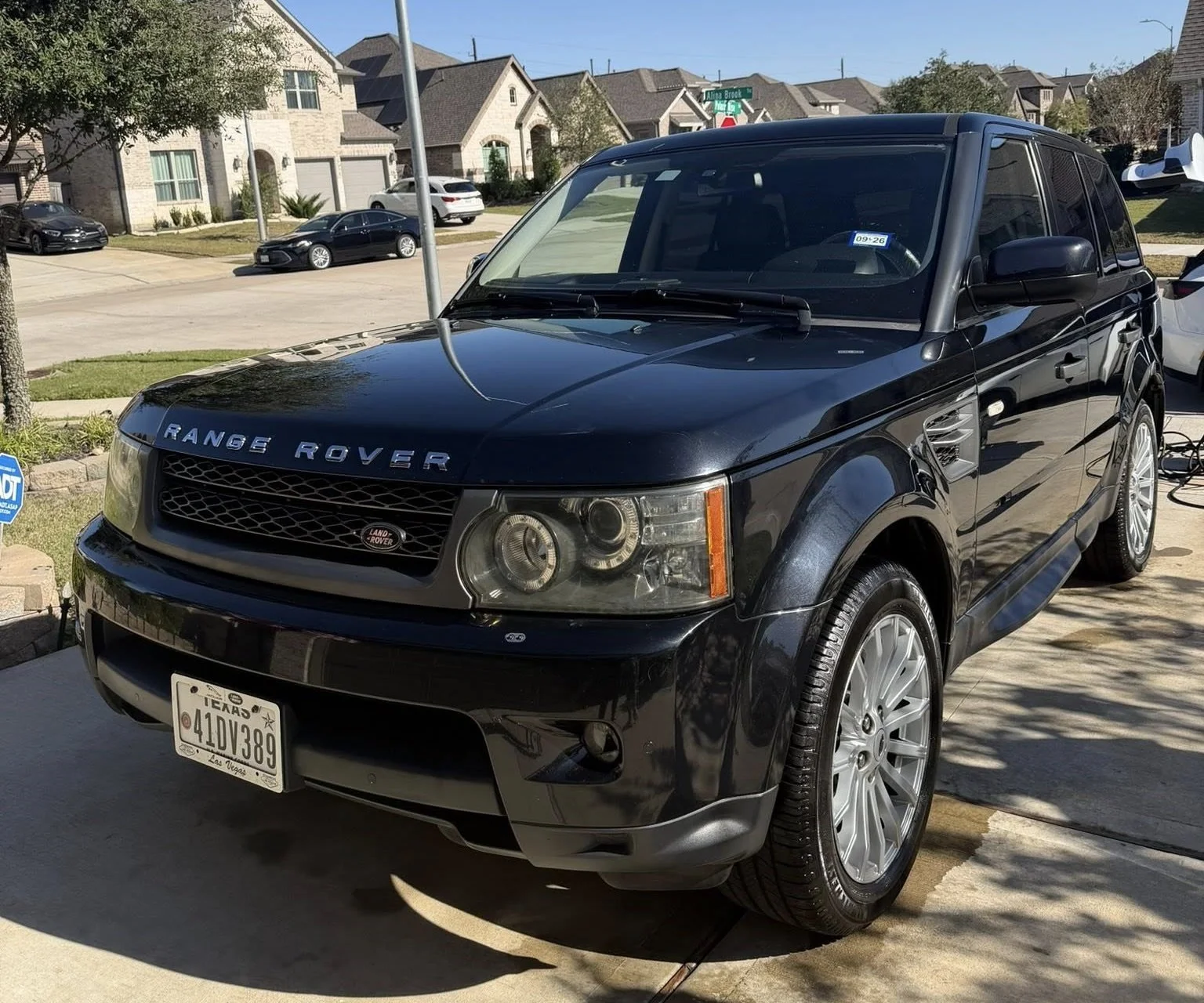 Black Range Rover SUV parked on a driveway in a suburban neighborhood with houses and trees in the background.