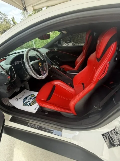 Inside a white sports car with red racing seats, black steering wheel with a clear cover, dashboard, and gear shift.