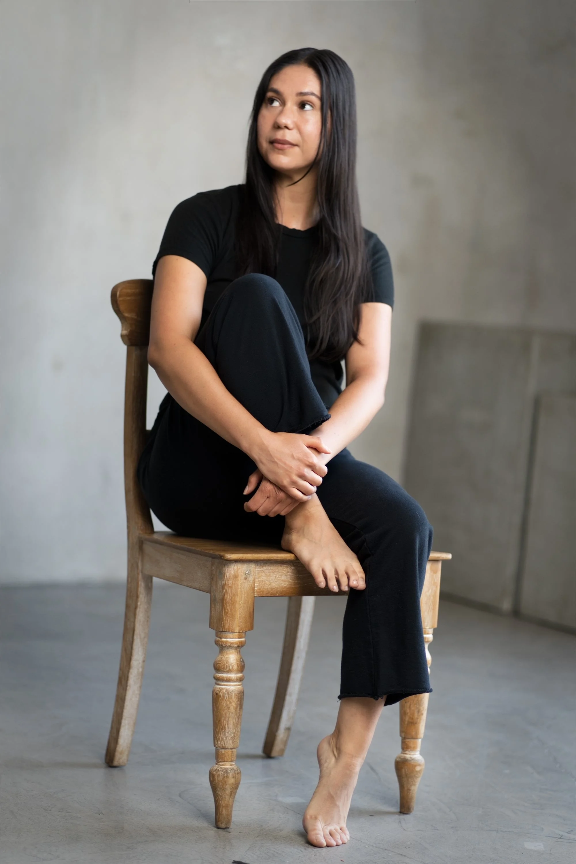 Portrait of a woman seated on a wooden chair against a neutral background.